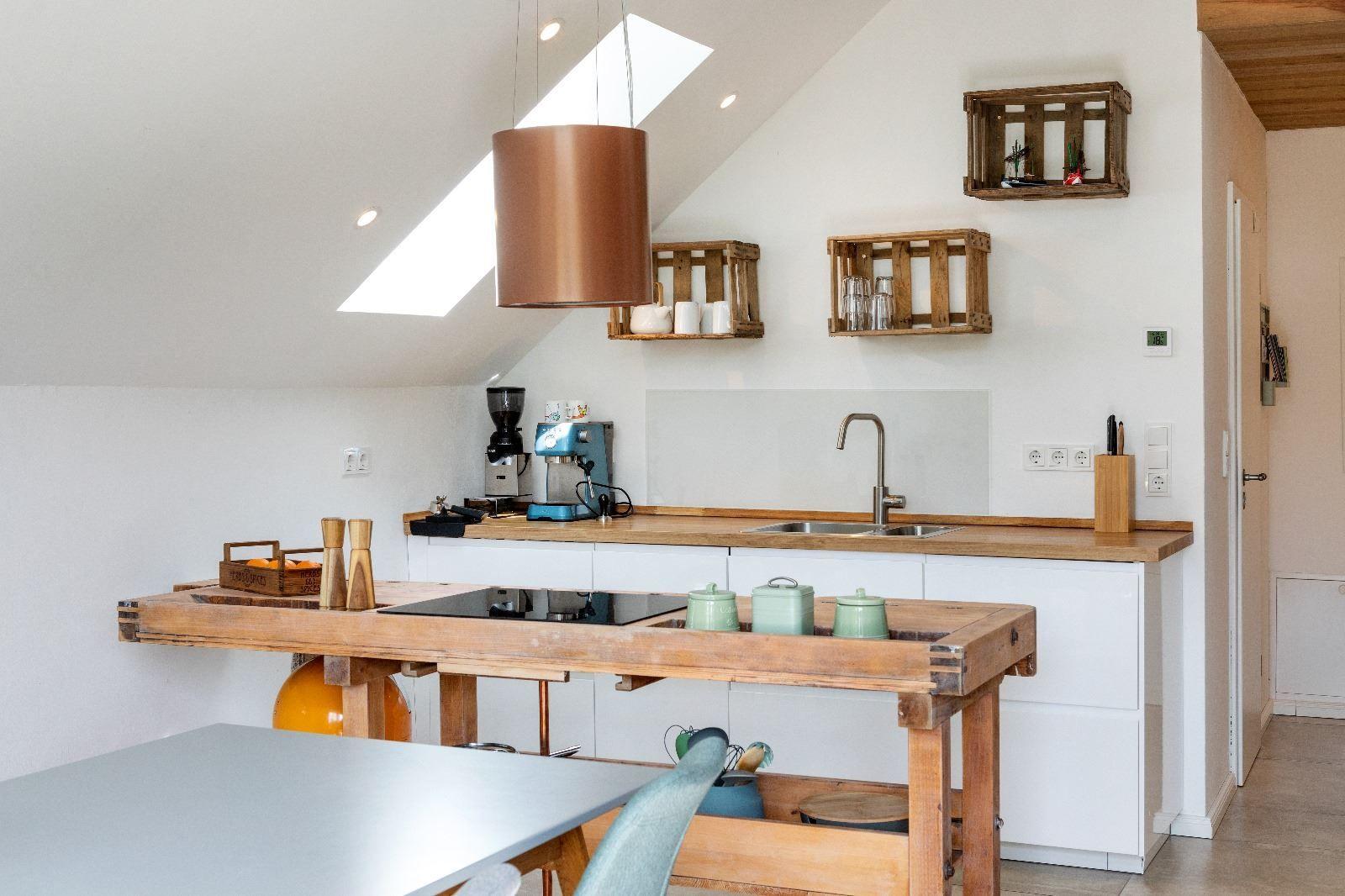 Küche mit Holztisch, weißen Schränken und Dachschrägen. An der Wand hängen Holzkisten.