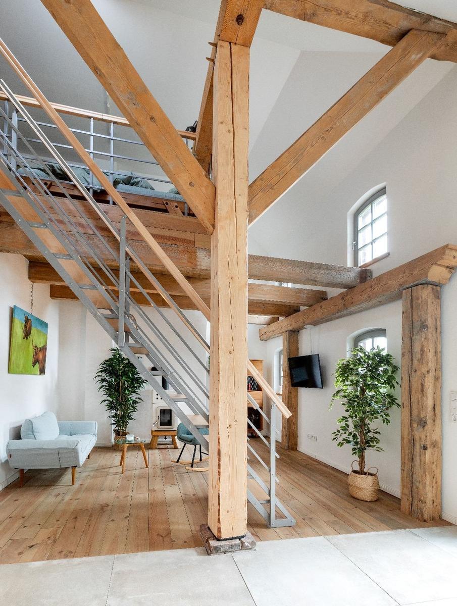Wohnraum mit Holzdeckenbalken, Metalltreppe und Pflanzen.