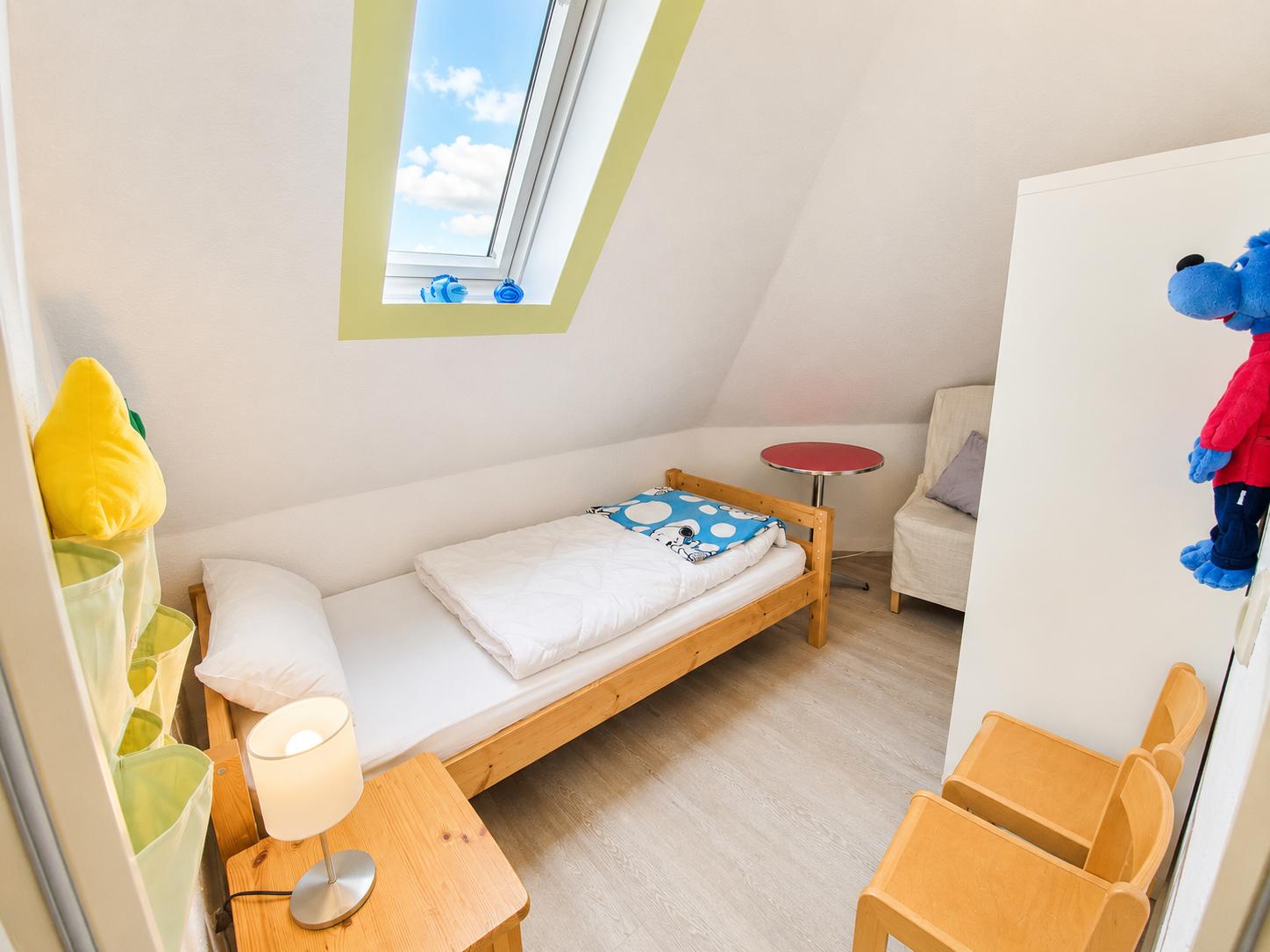 Ein Schlafzimmer mit Dachschräge, Bett, Stuhl, Tisch und Fenster.