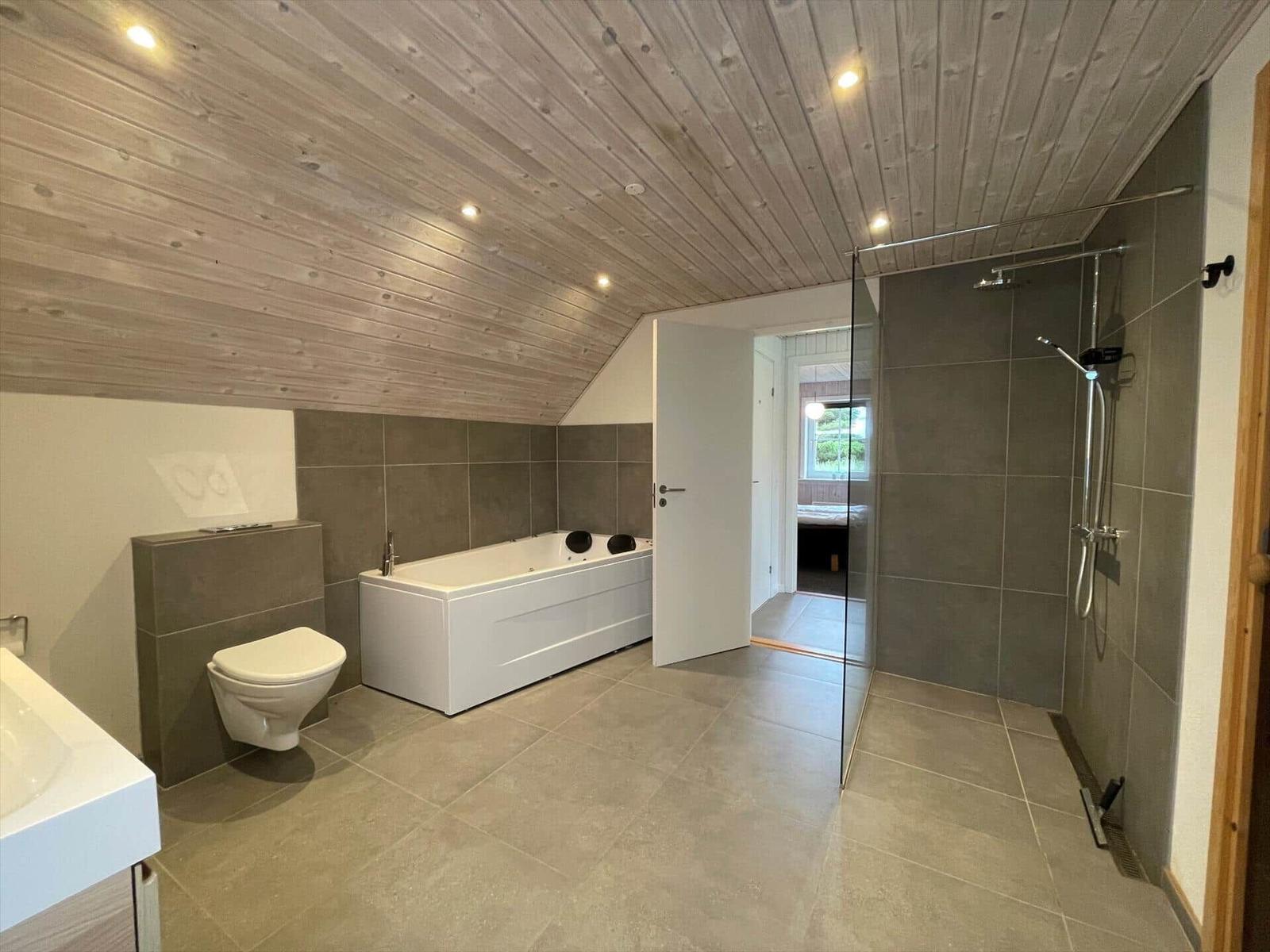 Badezimmer mit Badewanne, Dusche und Toilette unter Holzdecke.