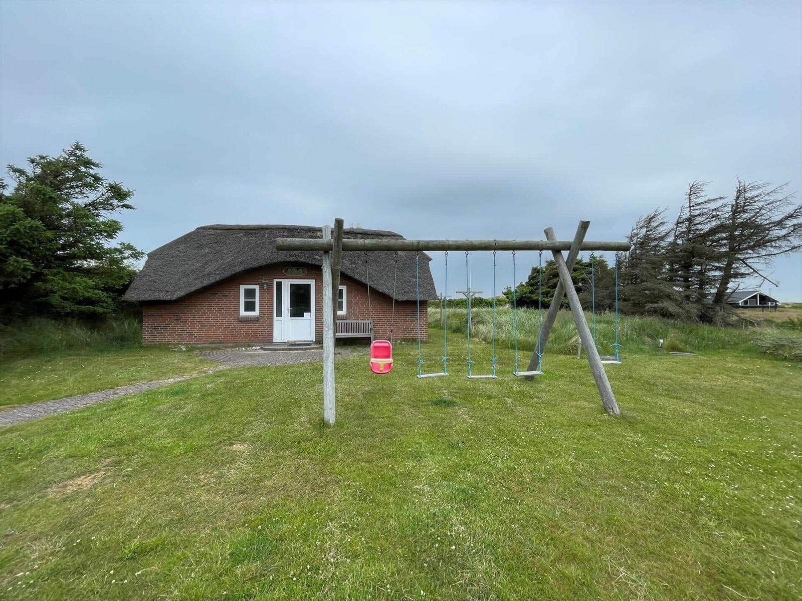 Haus mit Strohdach und Spielplatz mit Schaukel im Vorgarten.