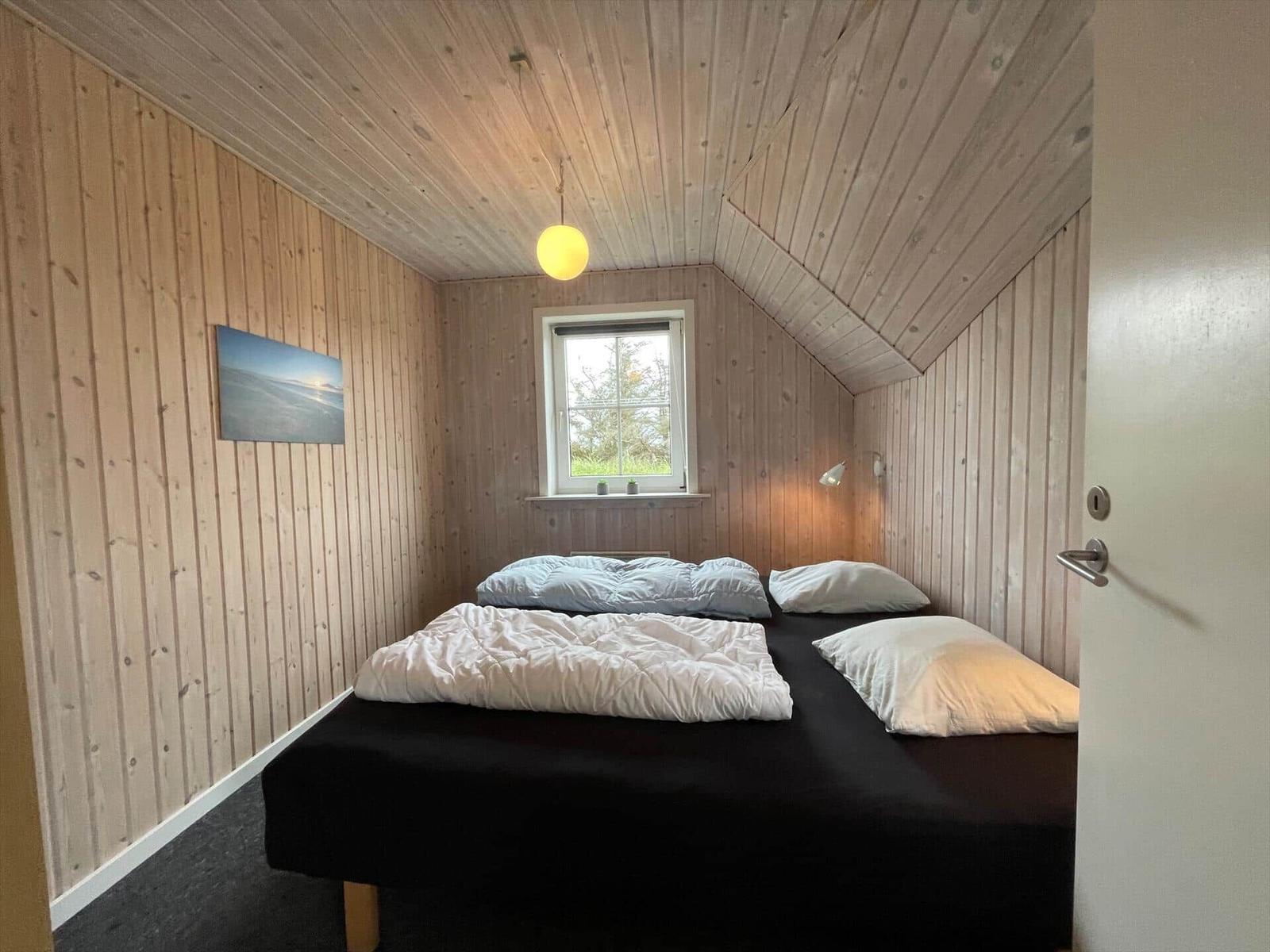Schlafzimmer mit Holzwand, Bett, Fenster und Deckenleuchte.