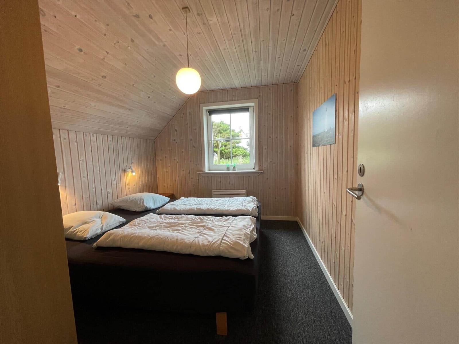 Schlafzimmer mit zwei Betten, Holzwänden und Fenster mit Blick nach draußen.