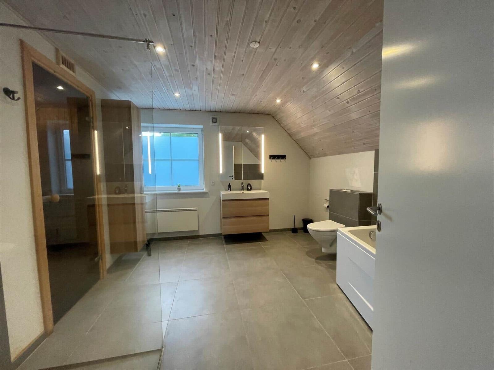 Moderne Badezimmer mit Dusche, Badewanne, Waschbecken und Toilette unter Holzdecke.