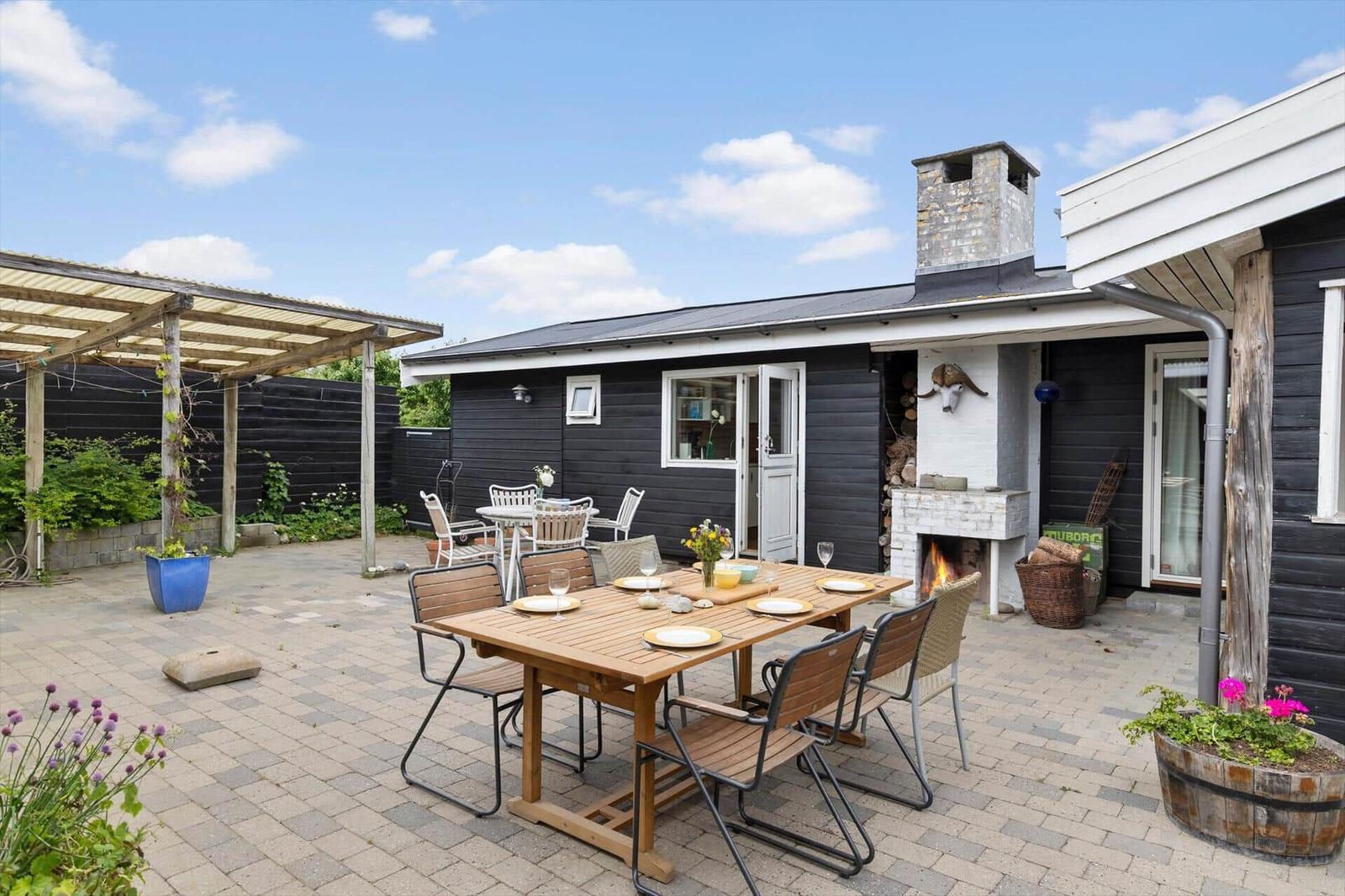 Hinterhof mit Tisch, Stühlen und Grill. Schwarze Holzwände und Pflanzen.