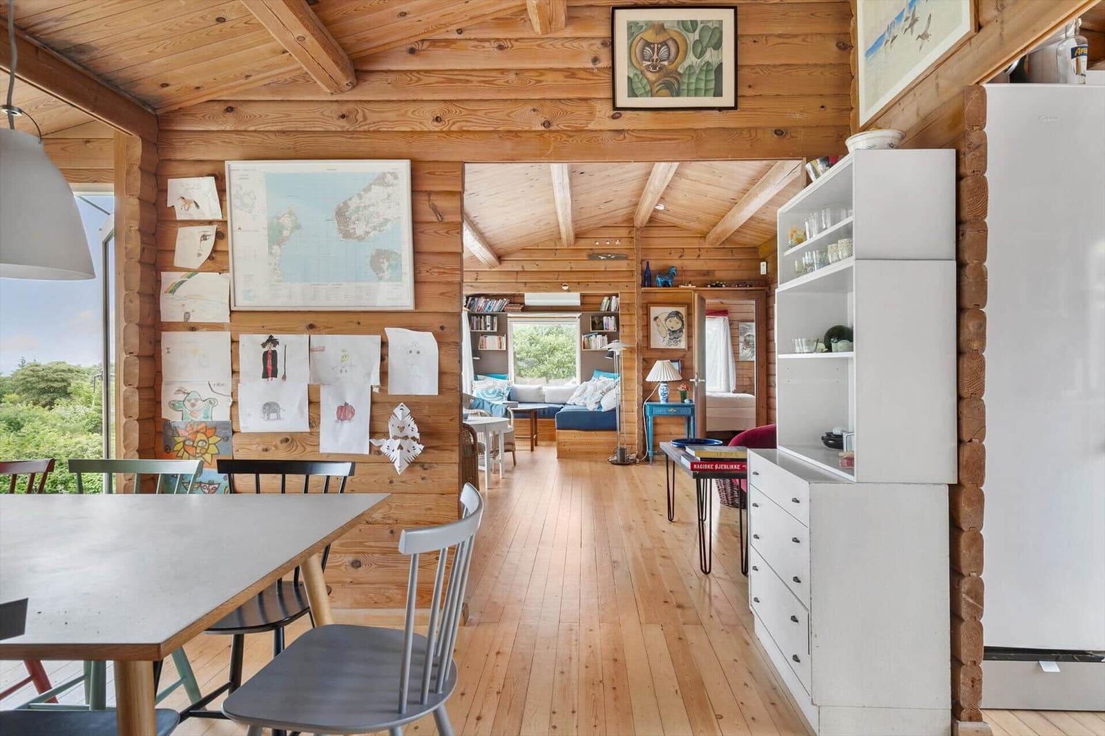 Holzhaus mit Essbereich, Wohnzimmer und Küchenzeile. Wand mit Kindergemälden und Karte.