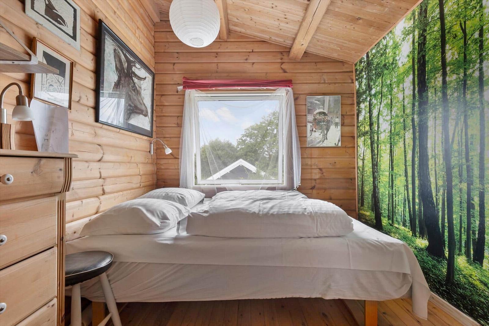 Schlafzimmer mit Holzwand, Bett, Fenster und Waldtapete.