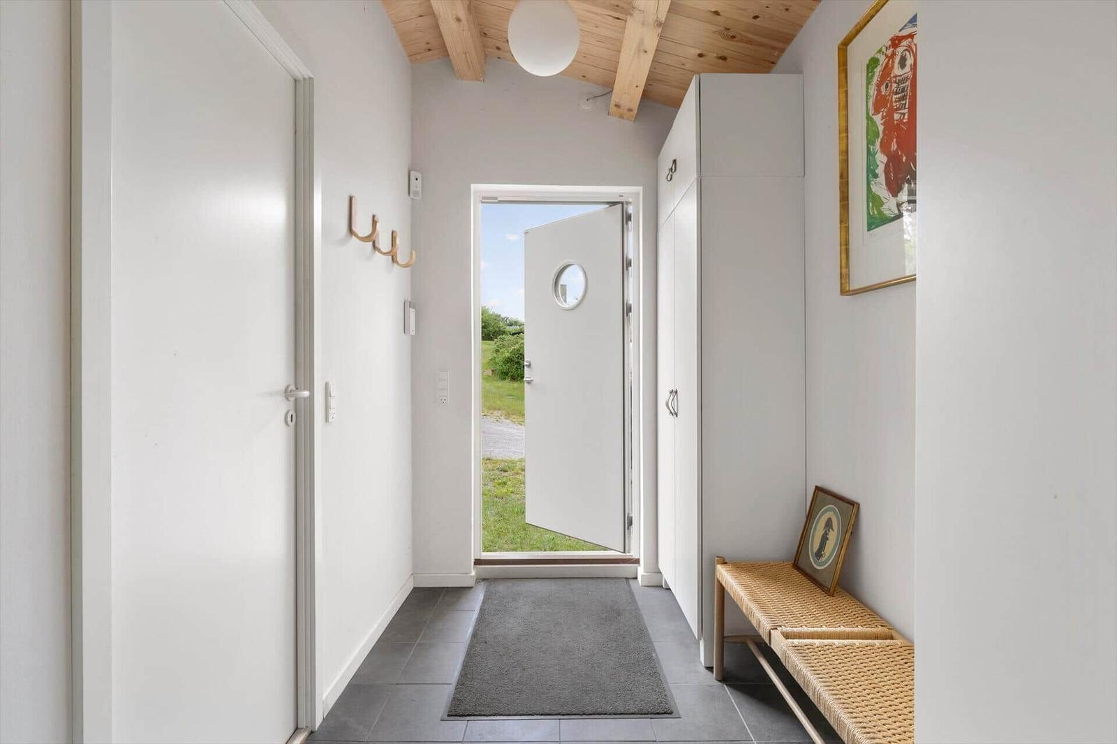 Eingangsbereich mit weißer Tür, Holzdecke und Schuhschrank. Durchgang zur Außentür.