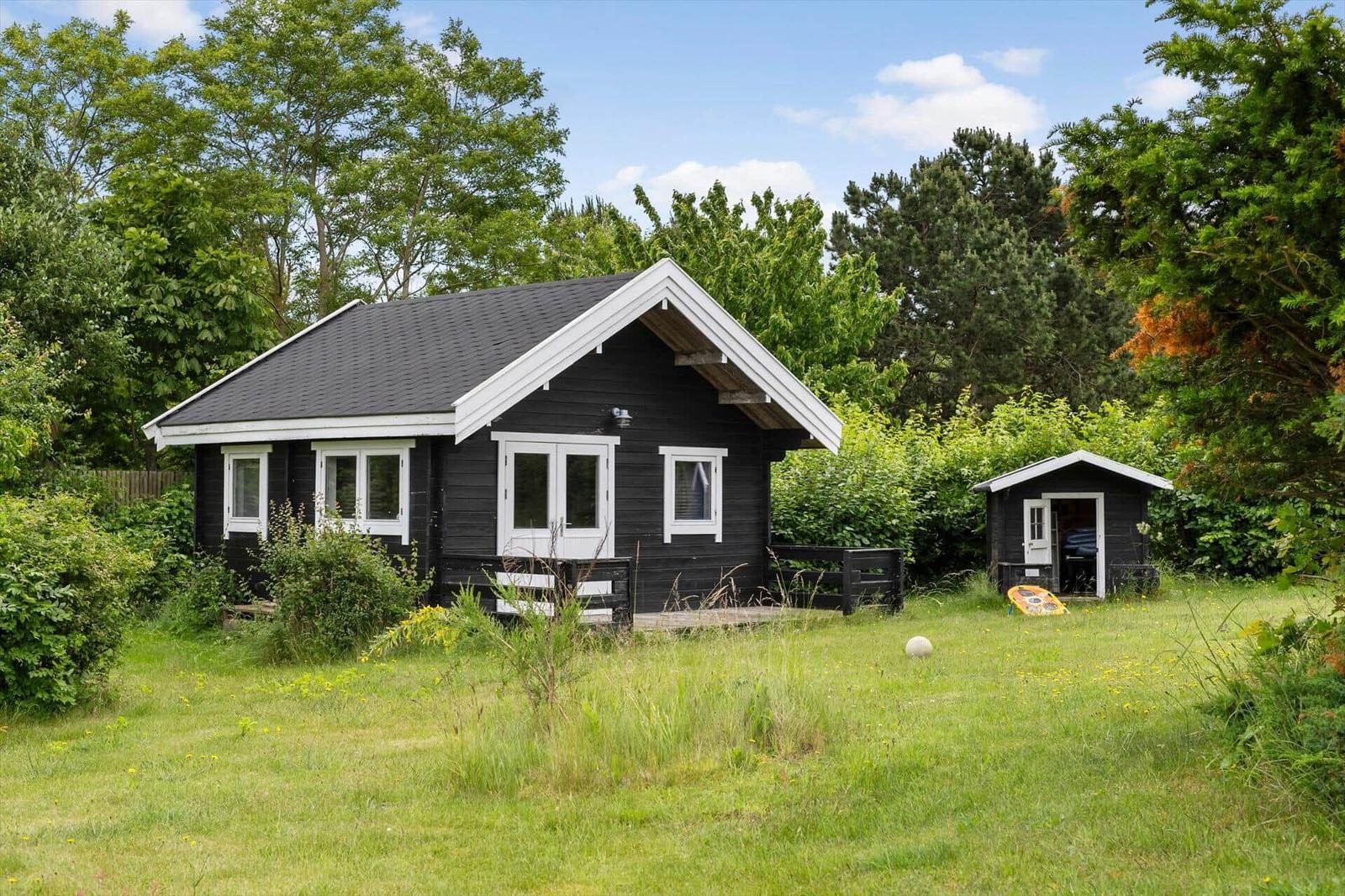 Schwarze Holzhütte mit weißen Fenstern und Terrasse im grünen Garten.