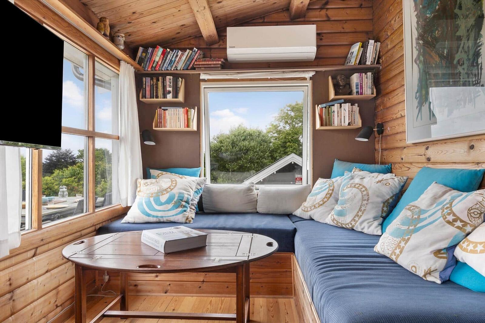 Ein Wohnbereich mit blauer Sitzbank, Holzwand und Bücherregalen. Ein runder Tisch steht im Zentrum.