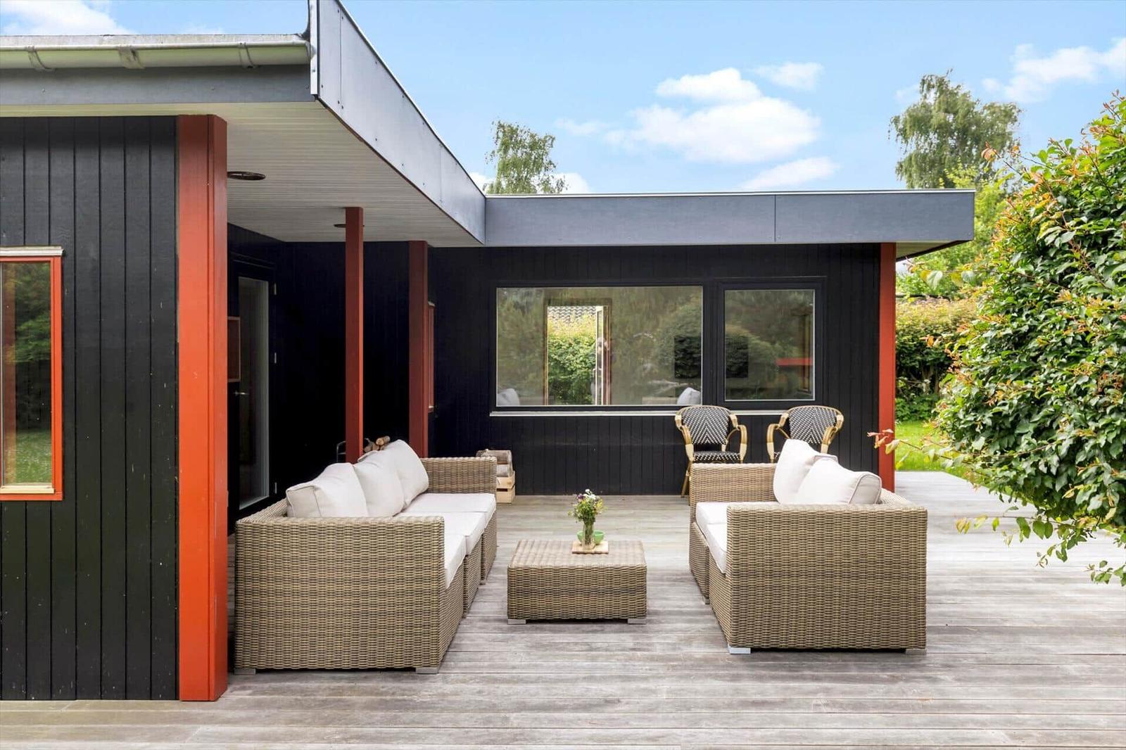 Deck with wicker sofa, table, and chairs. Black facade with red pillars.