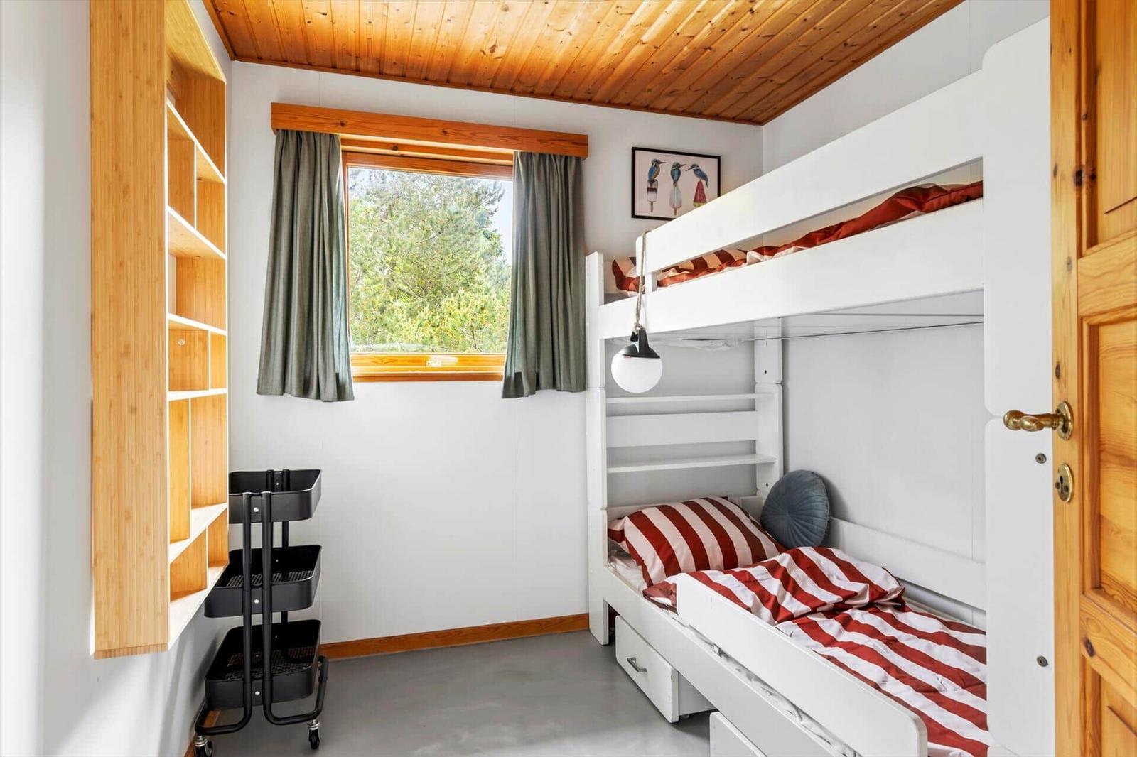 A bedroom with a bunk bed, a window, and a wooden shelf.