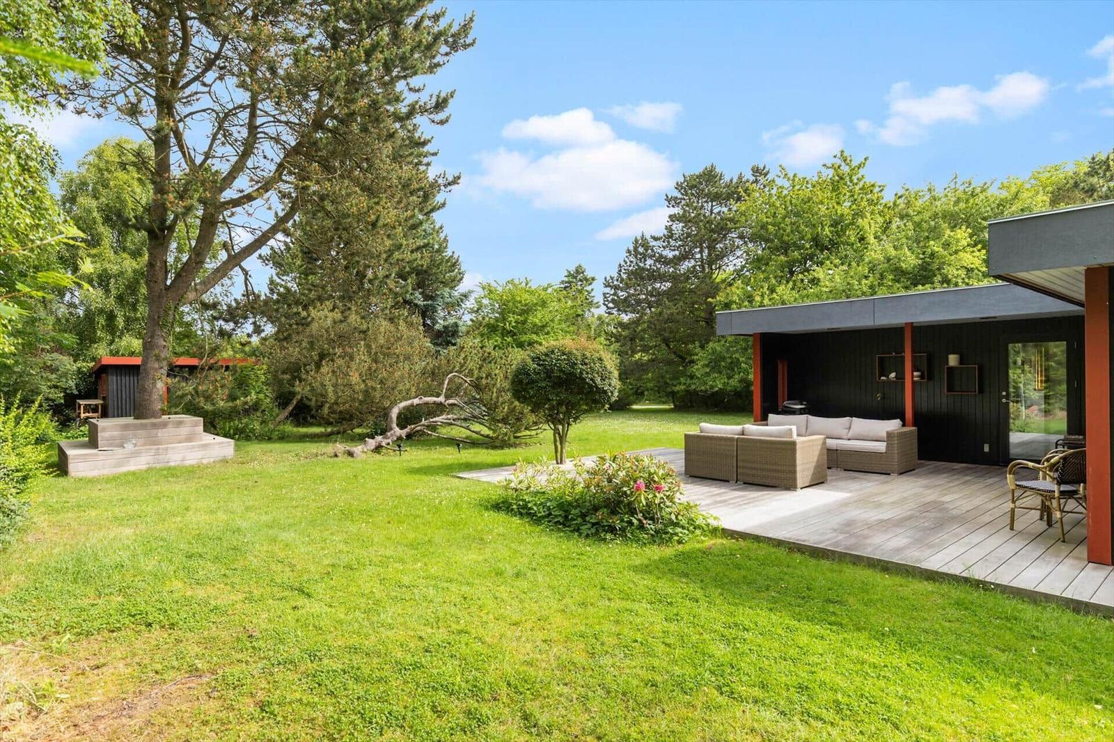 Deck with seating, large garden and trees under blue sky.