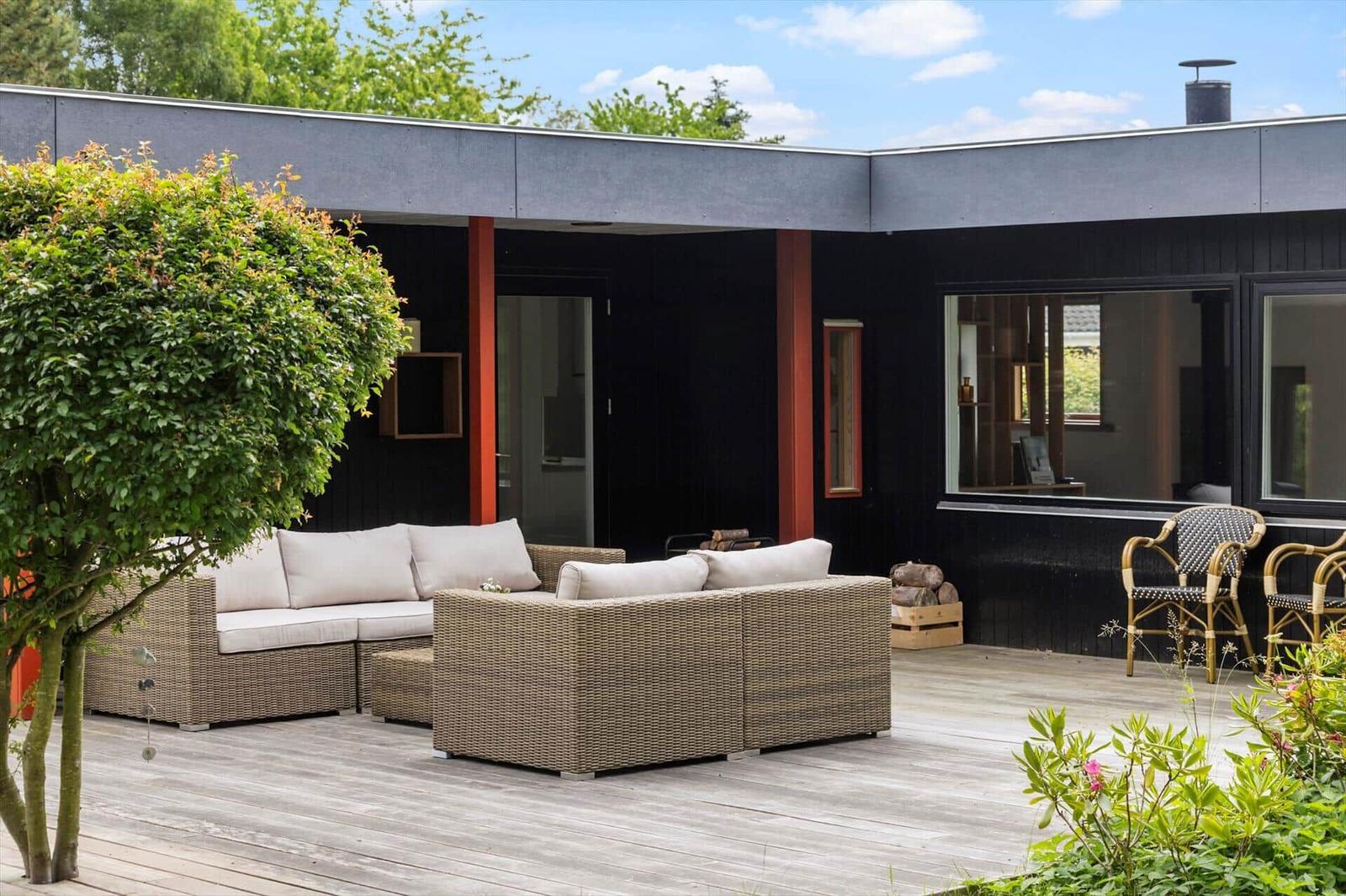Terrace with seating, wooden planks, and garden. Black facade with windows.