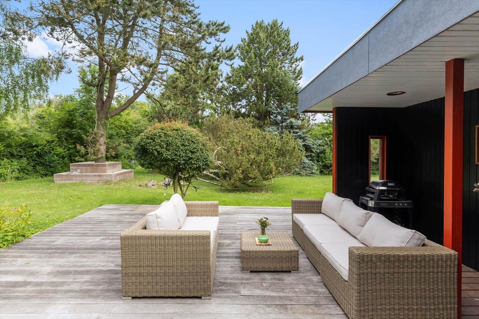 Deck with seating, grill and garden. Wooden floor, trees and grass visible.