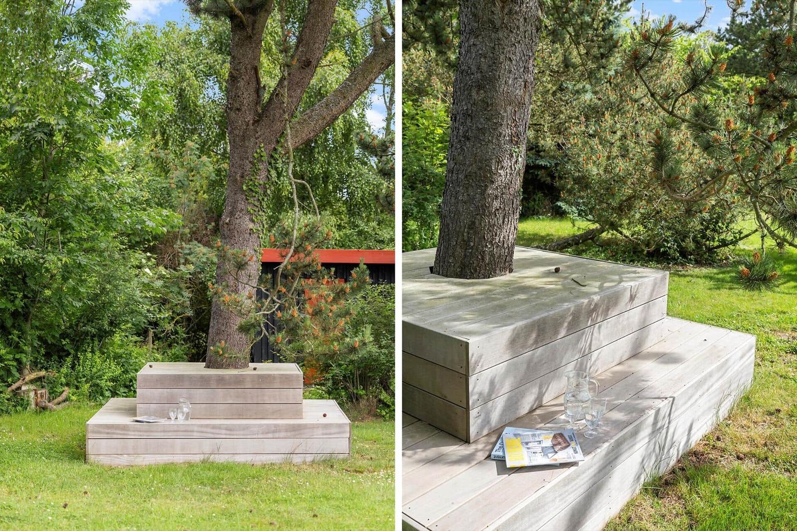 Wooden terrace around a tree with drinks and a magazine.