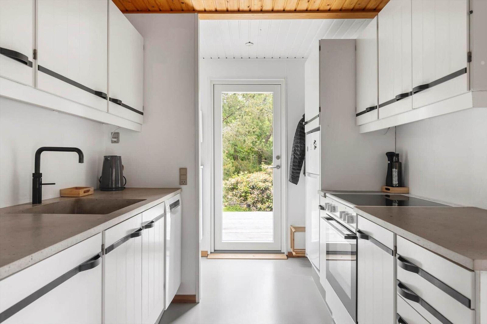 Kitchen with white cabinets, dark handles, and view to an outdoor area.