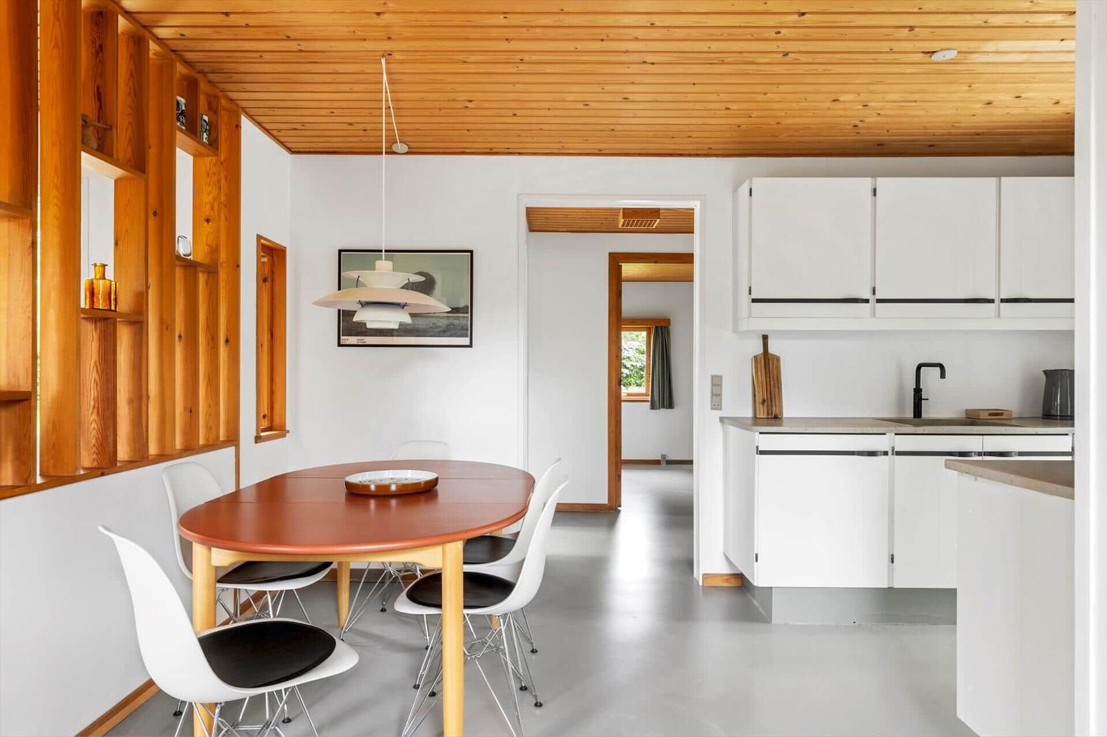 Kitchen and dining area with wooden ceiling, white built-in kitchen, and round table with chairs.