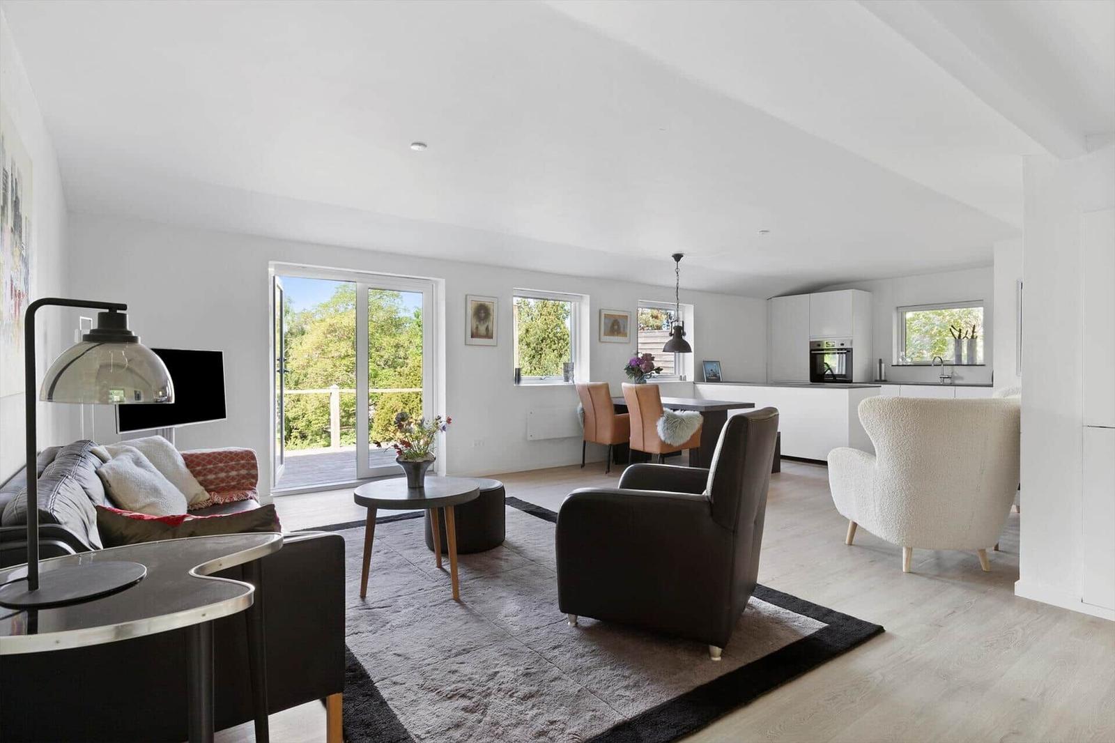 Living and dining area with kitchen, seating, and view to balcony.
