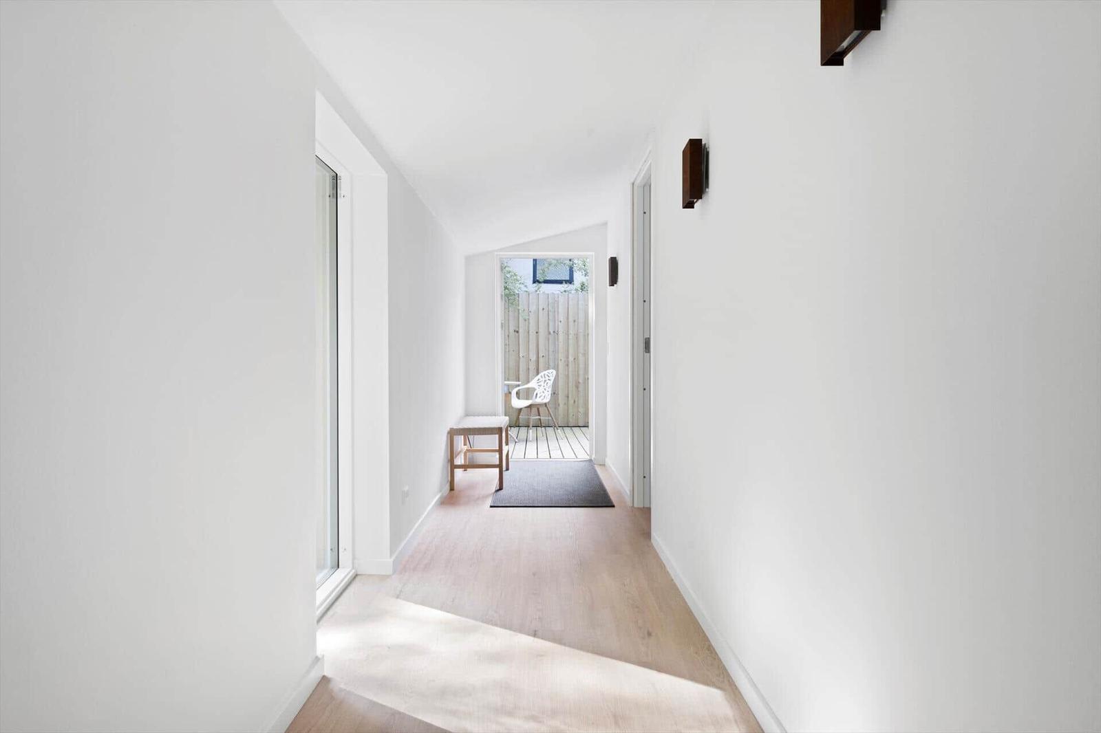 Hallway with wooden floor and window to terrace. White walls and wooden chair.