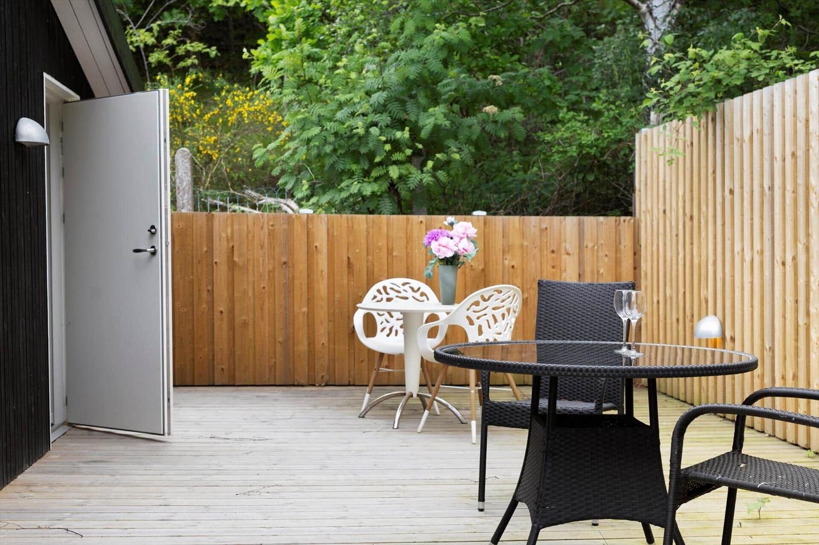 Deck with tables and chairs, wooden fence, and plants in the background.