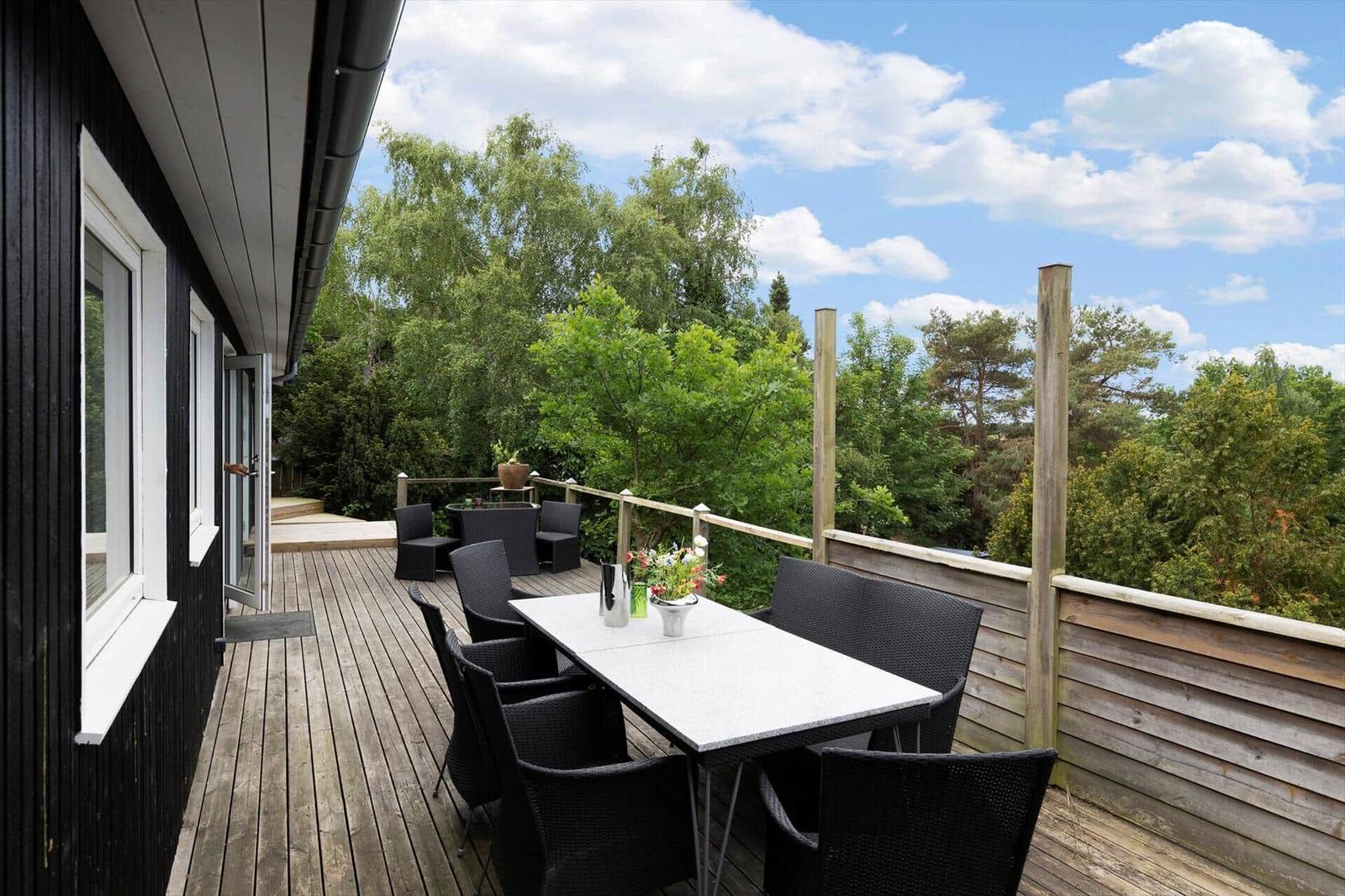 Deck with table and chairs, view of green trees under blue sky.