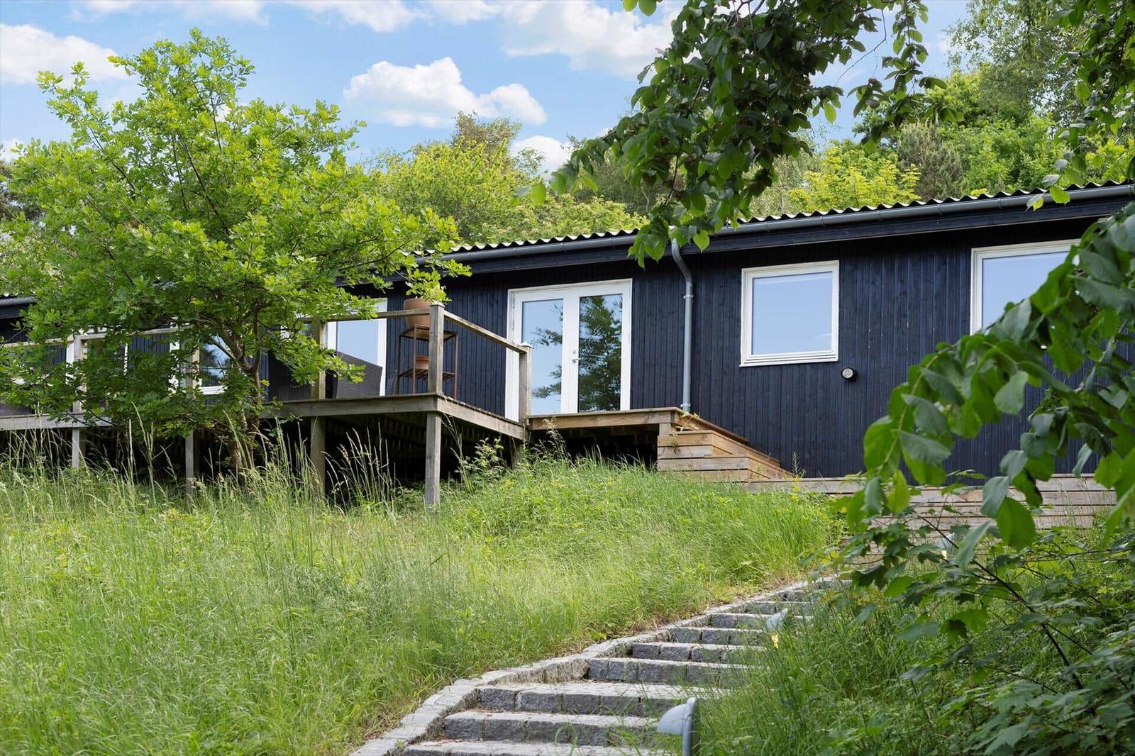 A dark blue house with a terrace and steps through grass. Surrounded by trees and greenery.