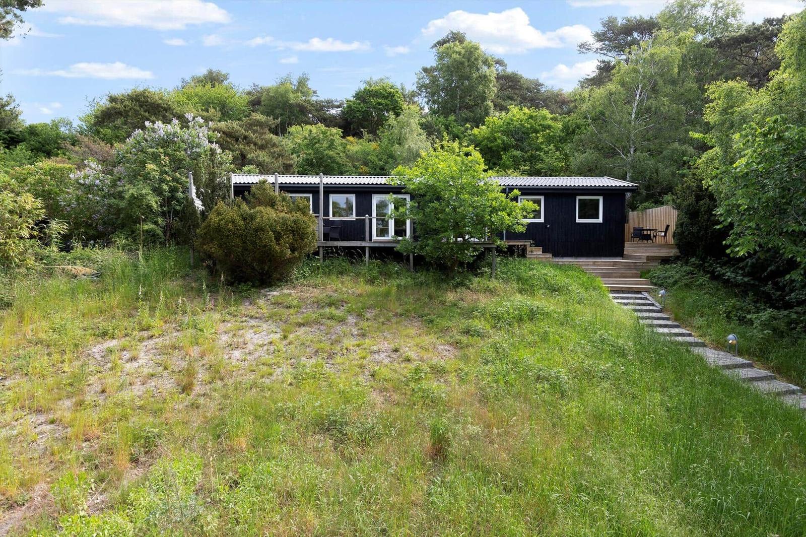Black wooden house with terrace and garden. Surrounded by trees and grass.