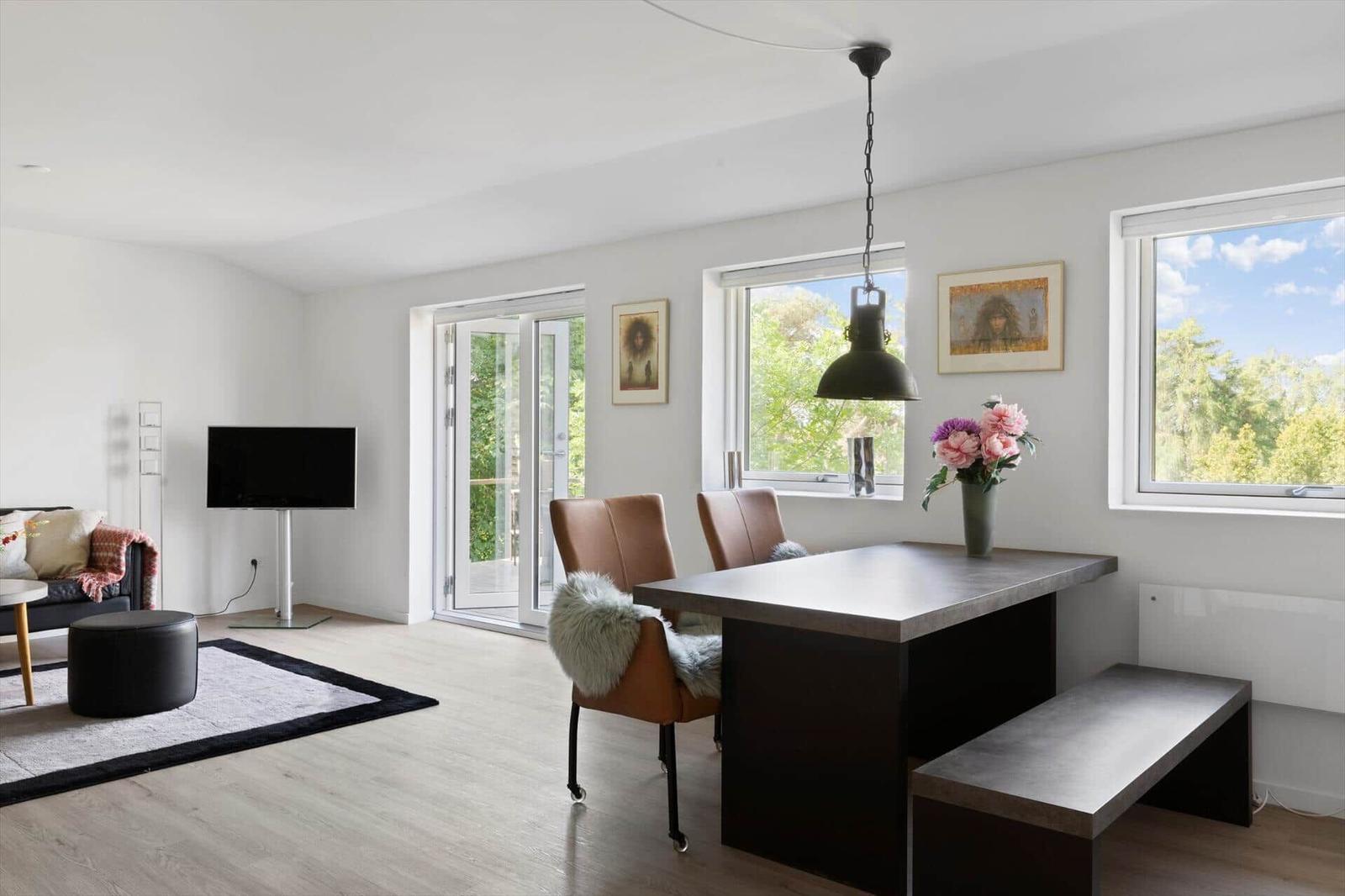 Dining area with table, chairs, and windows. Living area with sofa, TV, and hallway.