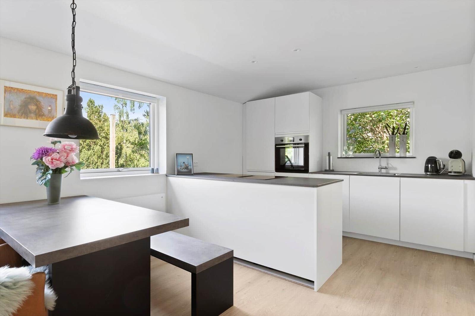 Modern kitchen with white cabinets, kitchen island, and windows with view of greenery.