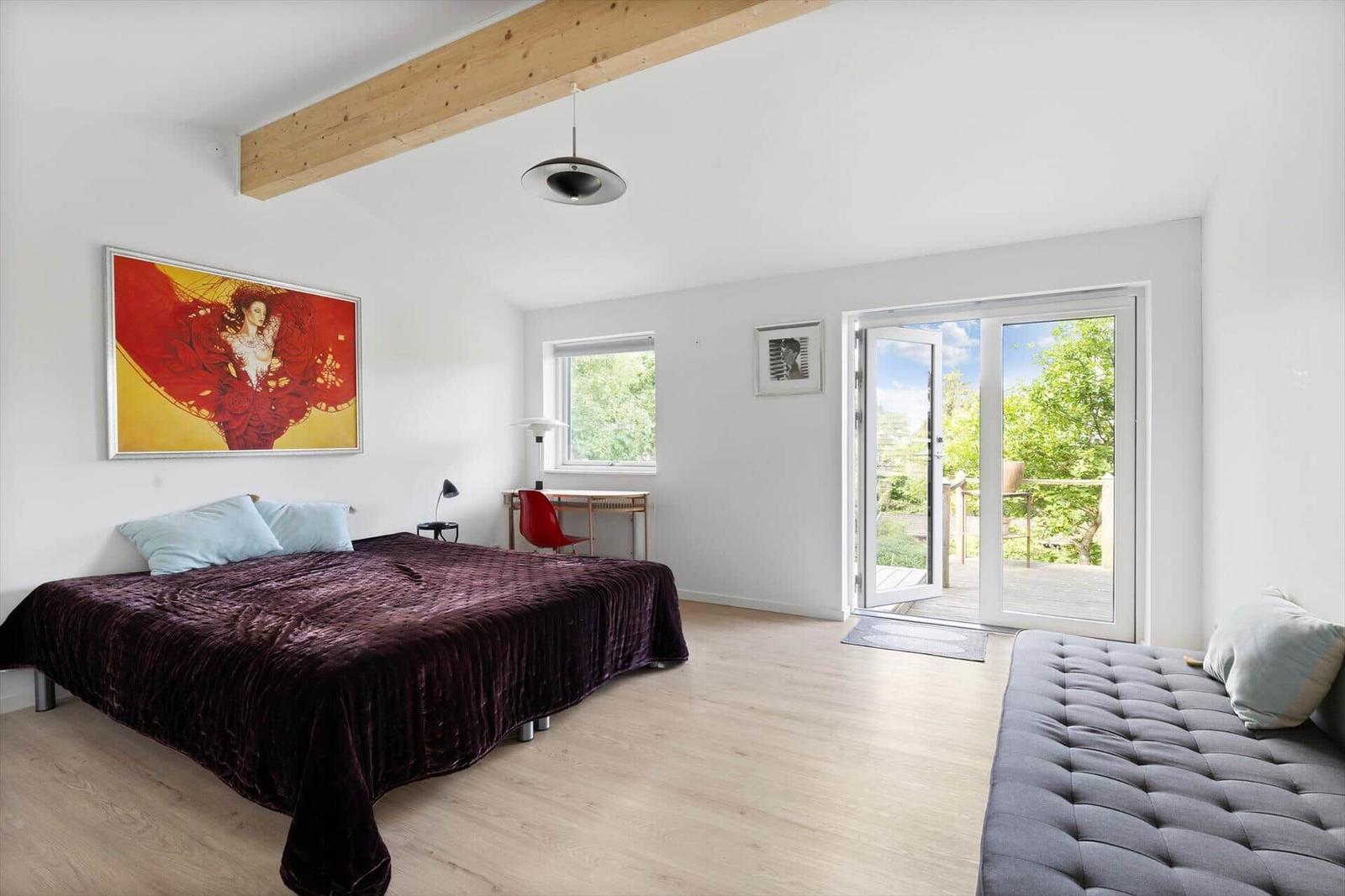 Bedroom with bed, bench, and balcony door. Visible wooden beam and wall art.