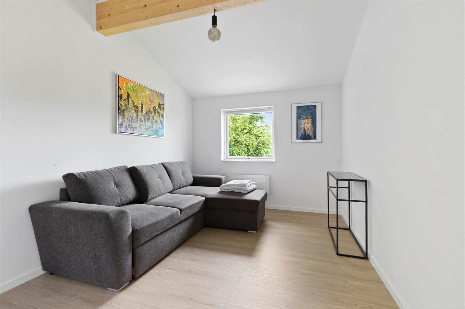 Living room with gray sofa, wooden floor, and window with view of trees.