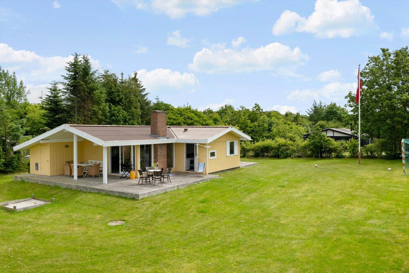 Ein gelbes Ferienhaus mit Terrasse und Garten. Daneben steht eine dänische Flagge.