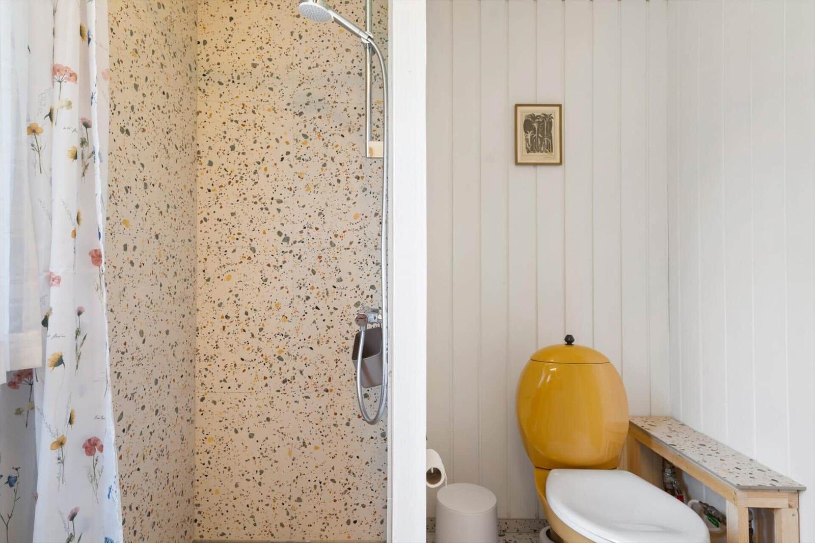 Bad mit Dusche, gelbem WC und floraler Duschvorhang.