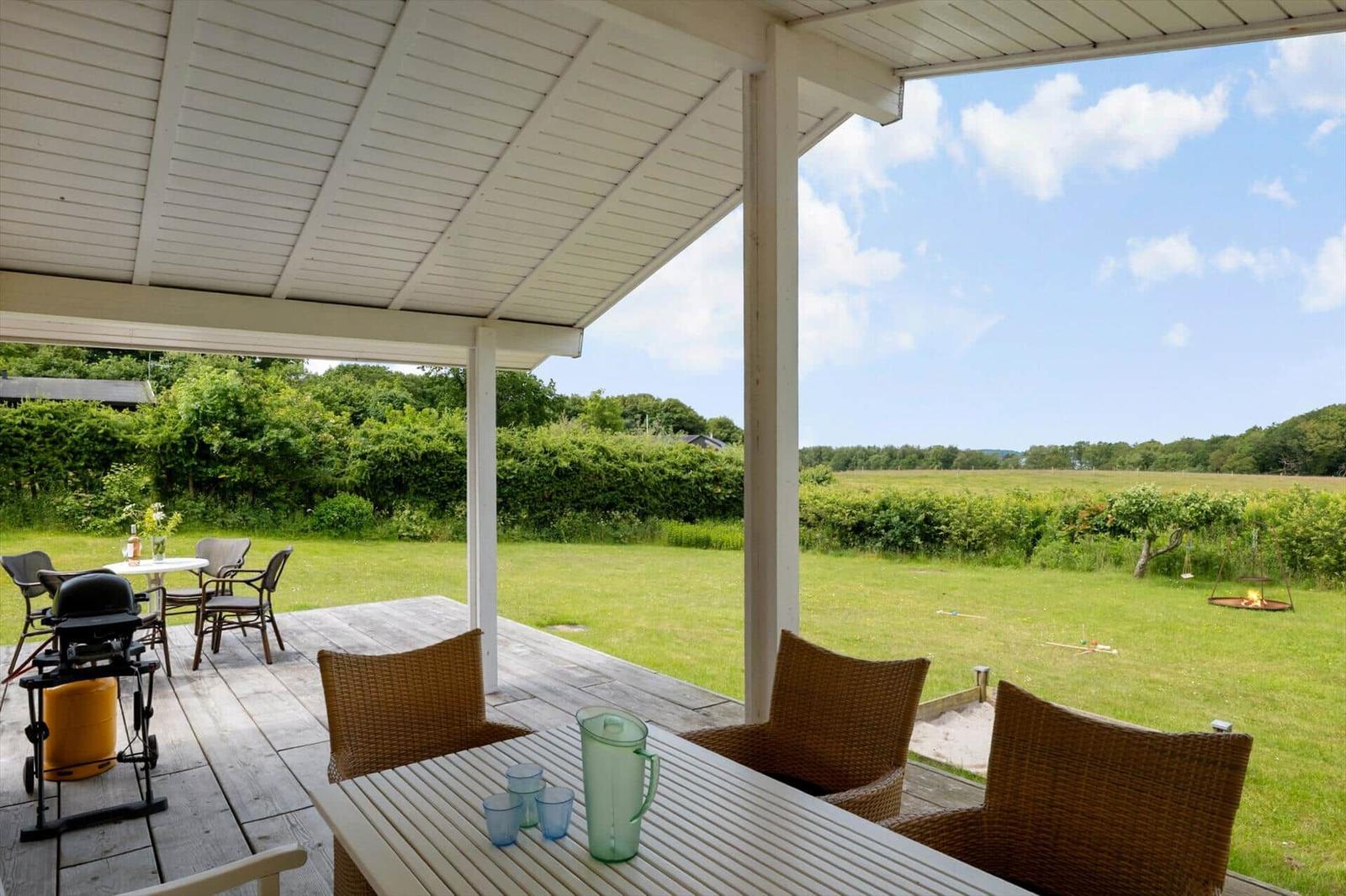 Terrasse mit Tisch und Stühlen, Grill und Blick auf grünes Feld.