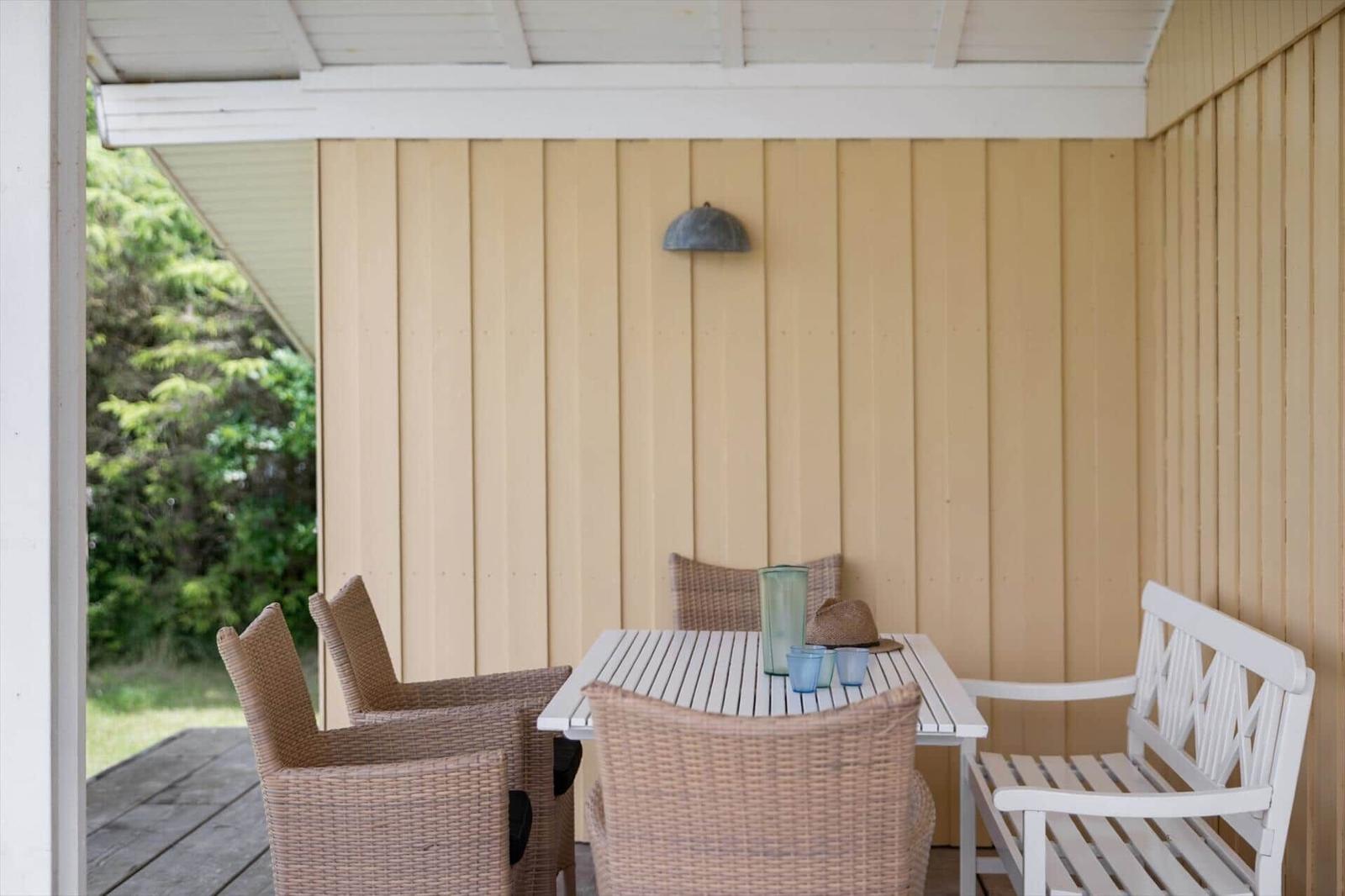 Terrasse mit Tisch, Stühlen und Bank. Hintergrund: Holzwand und grüne Vegetation.