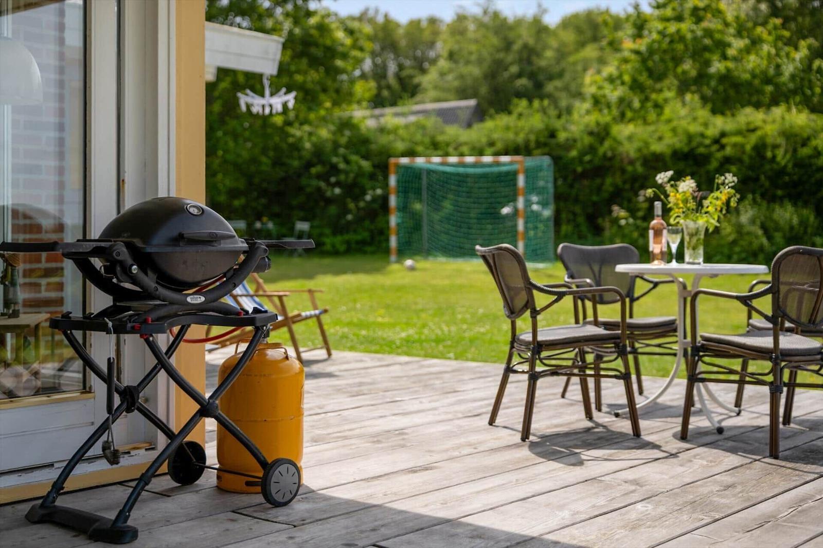 Terrasse mit Grill, Tisch und Stühlen. Im Hintergrund Fußballtor und Grünfläche.