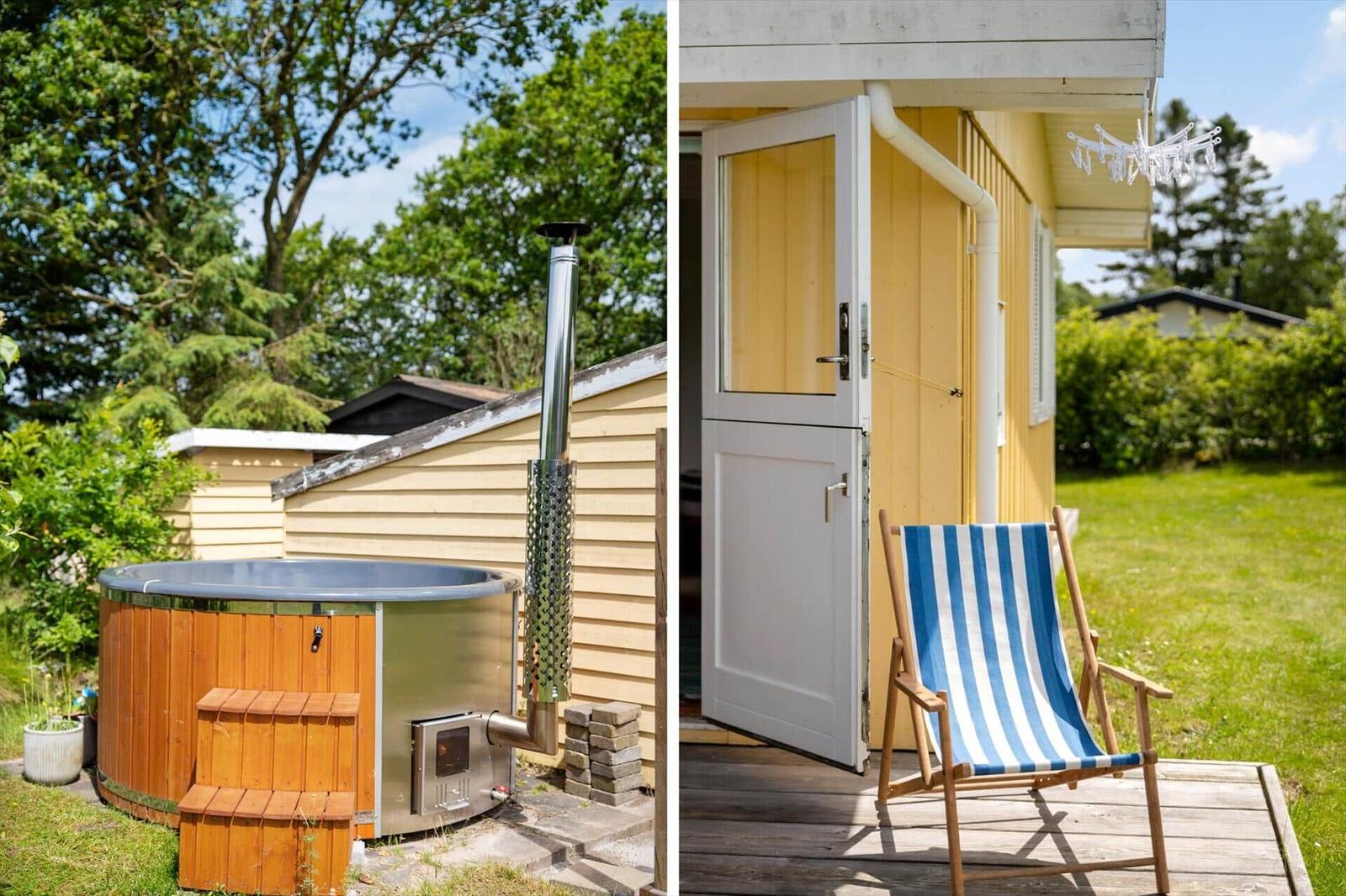 Hütte mit Whirlpool und Strandliege auf Terrasse. Umgeben von Grün und Bäumen.