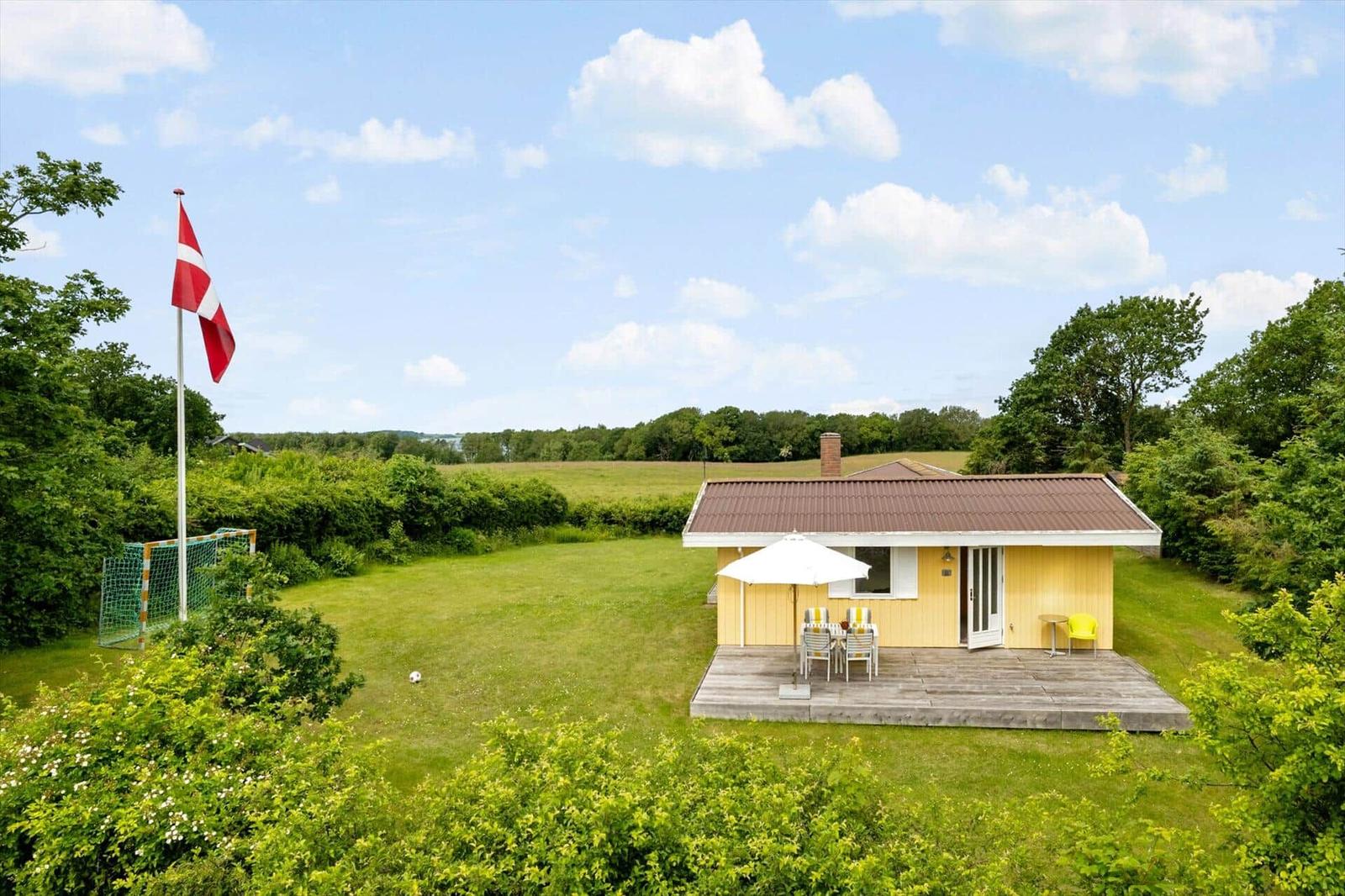 Gelbes Haus mit Terrasse, weißem Sonnenschirm und Garten. Daneben steht eine dänische Flagge.