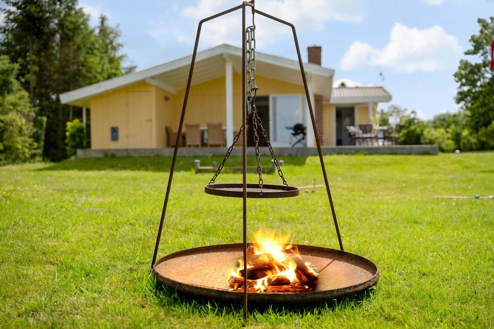 Feuerkessel mit hängendem Grillrost auf Rasen vor Ferienhaus