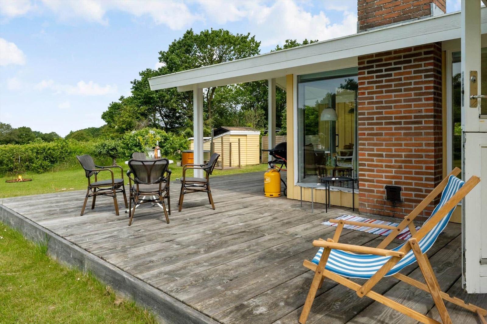 Holzterrasse mit Gartenmöbeln, Grill und Sicht auf grüne Landschaft.