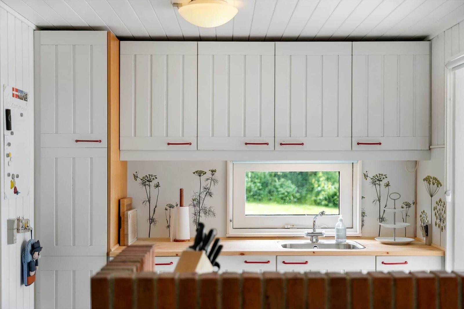 Küche mit weißen Schränken, Holzoberfläche und Fenster zur grünen Außenseite.