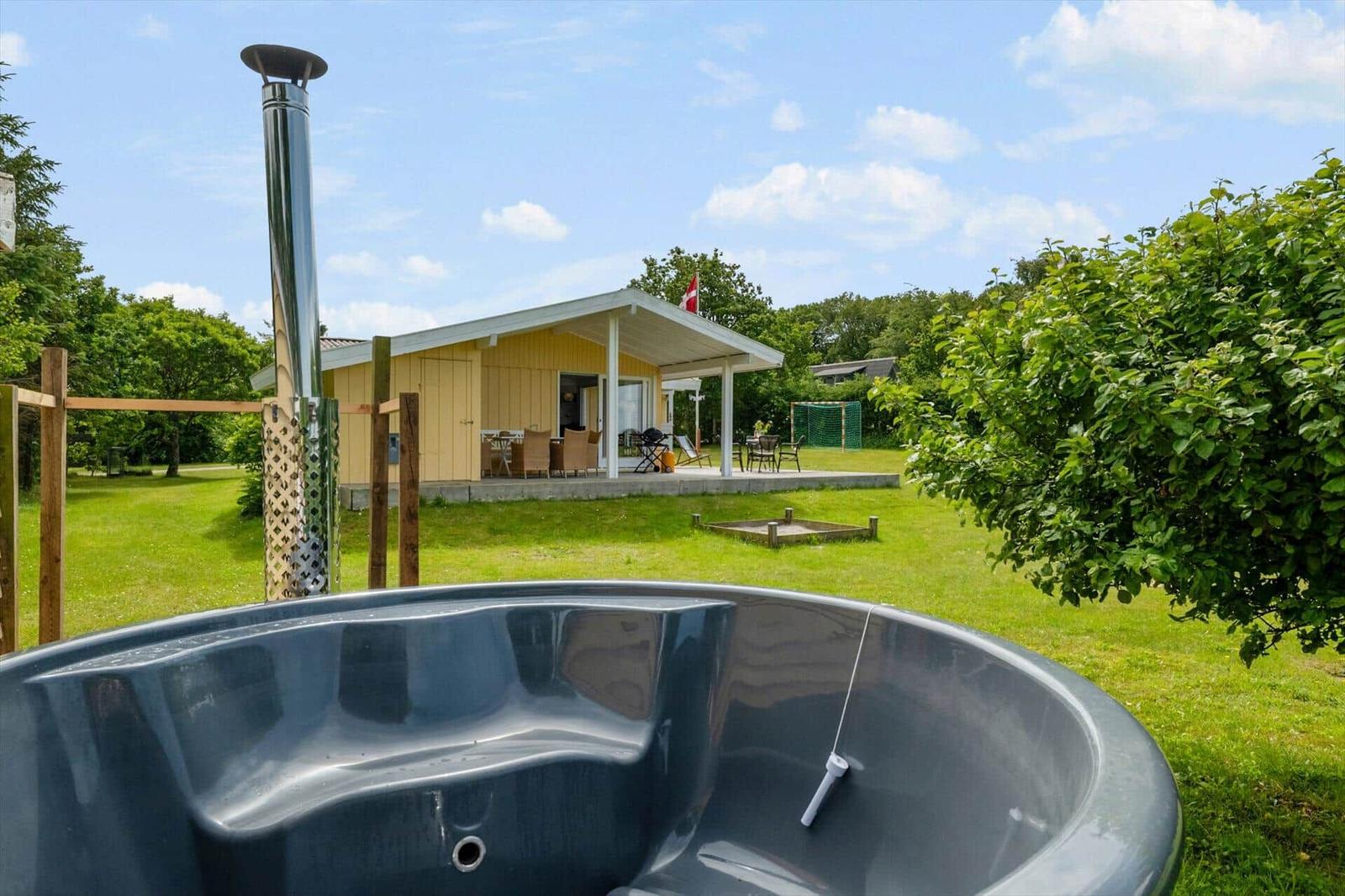 Hütte mit Whirlpool und Terrasse im Grün. Dänische Flagge weht.