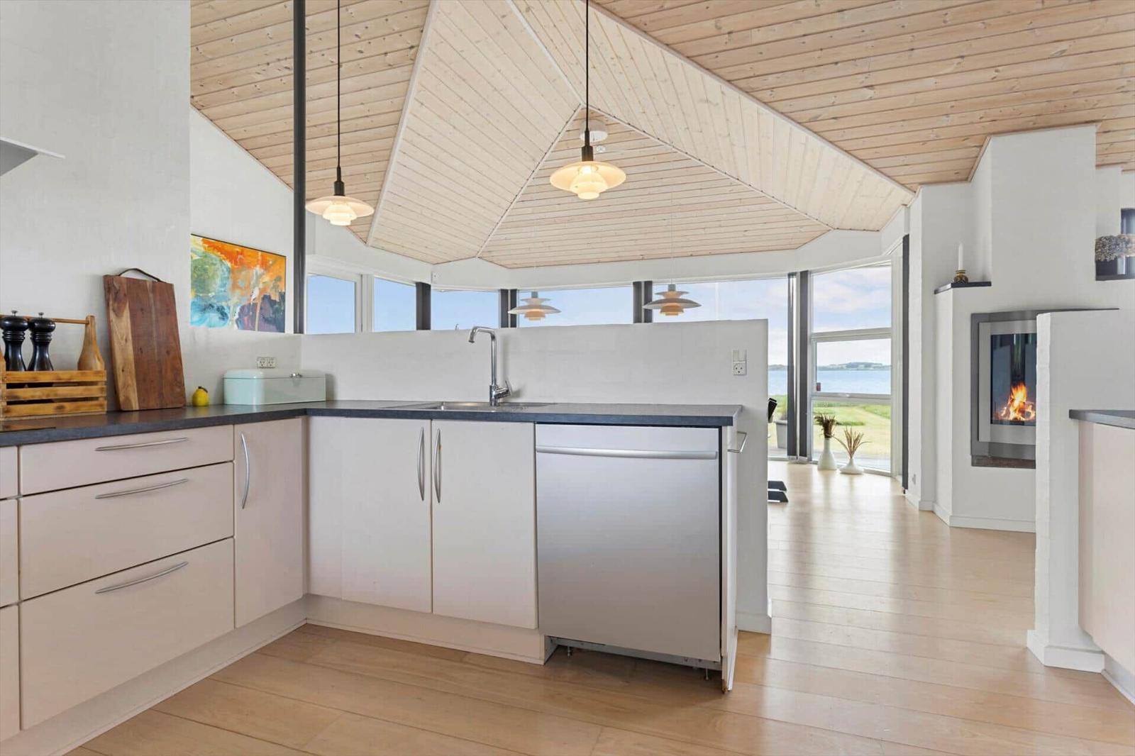 Küche mit Edelstahlspüle und Waschmaschine, Holzdecke und Blick aufs Meer.