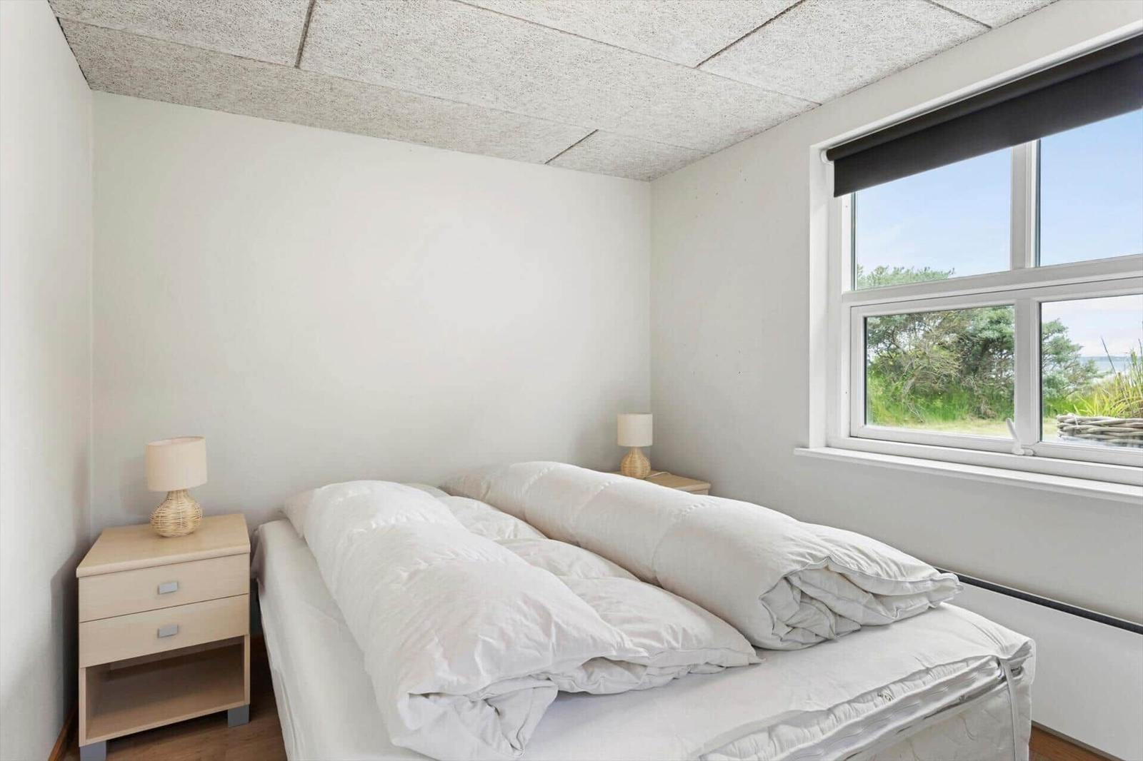 Schlafzimmer mit Bett, zwei Nachttischen und Fenster mit Blick auf Grün.
