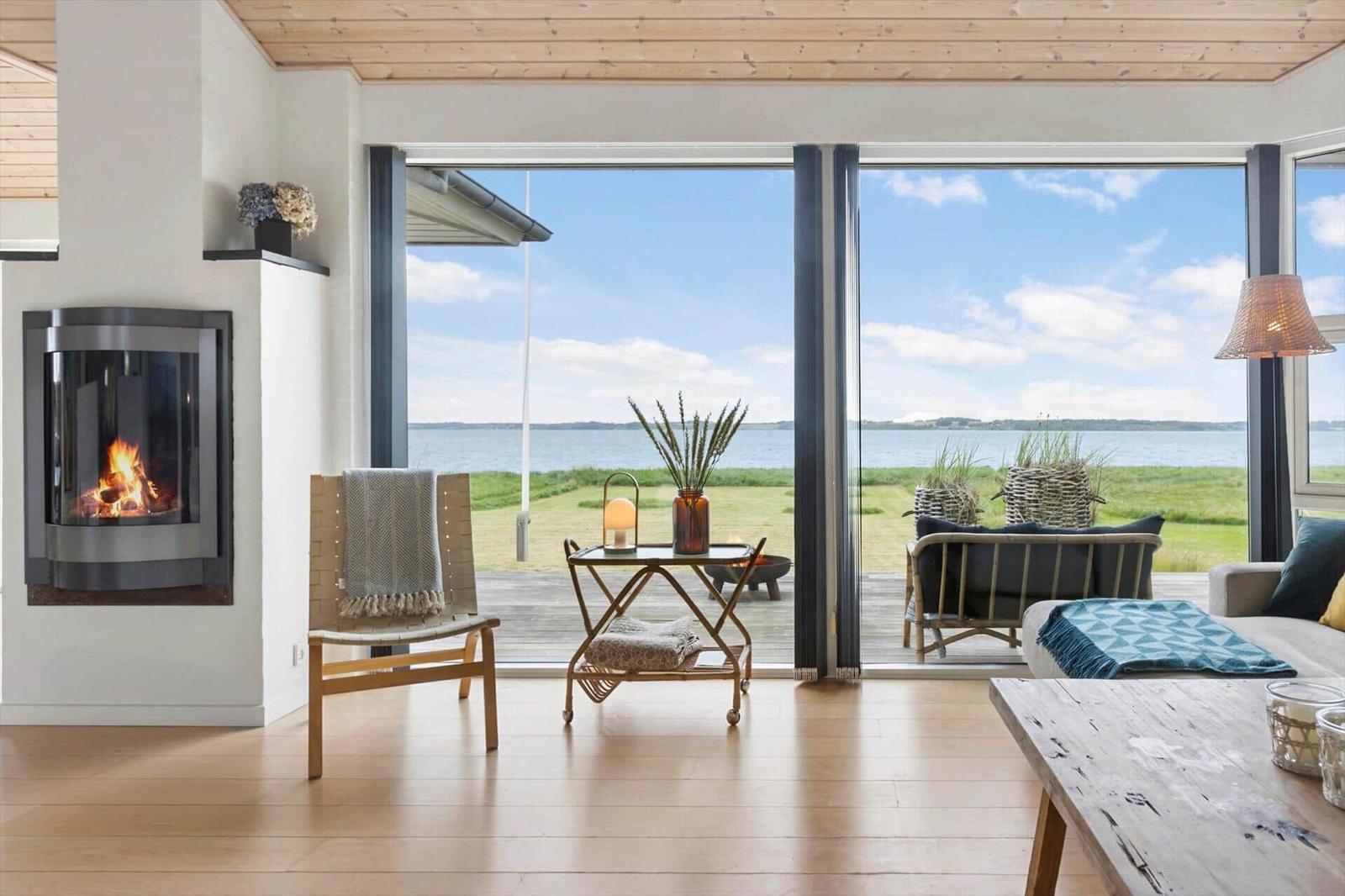 Wohnraum mit Kamin, Sitzgelegenheiten und Blick auf Wasser und Gras.