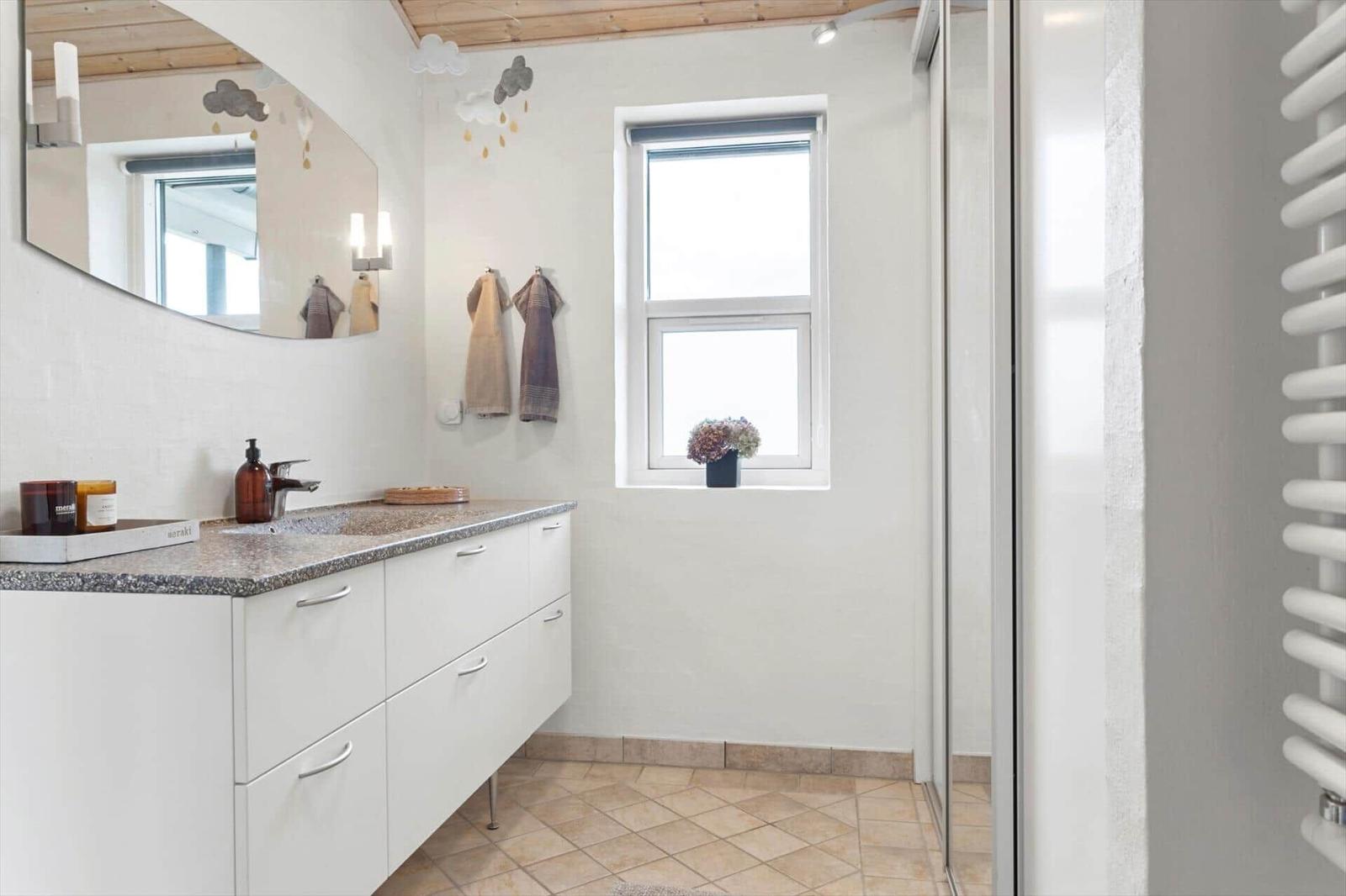 Badezimmer mit Waschtisch, Spiegel und Dusche. Fenster mit Blumen.