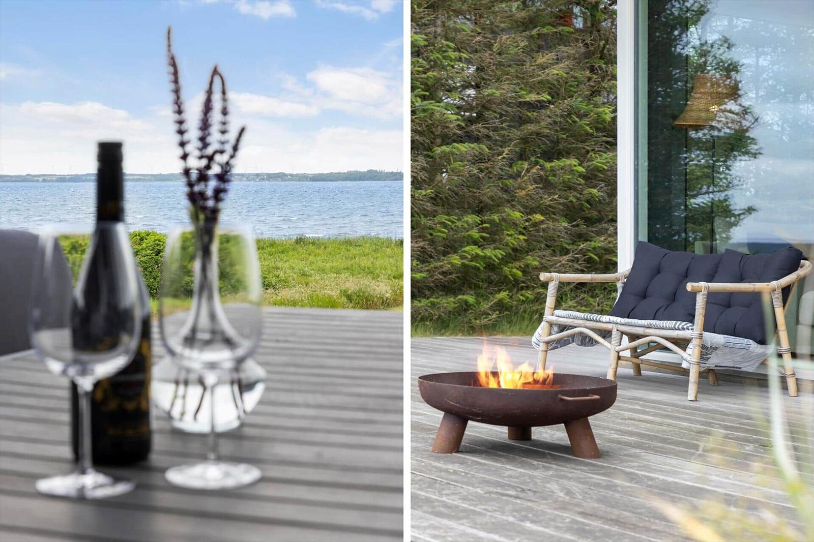 Tisch mit Wein und Blumen am Wasser. Feuerkorb und Sitzgelegenheit auf Terrasse.