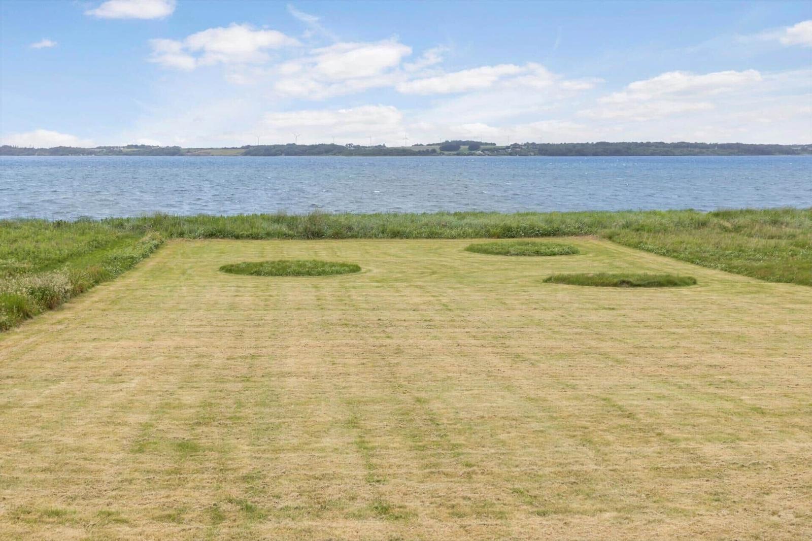 Grüner Rasenbereich mit drei runden Grasflächen am Wasser.
