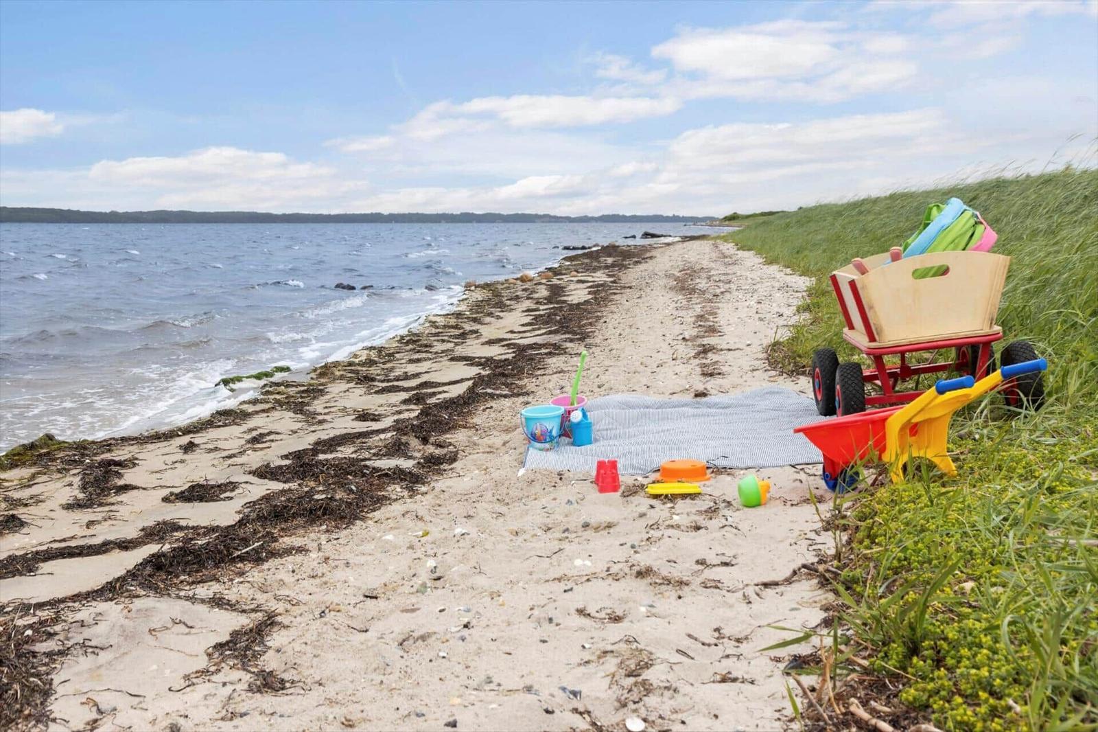 Strand mit Kinderspielzeug und Picknickdecke. Wasser und Gras im Hintergrund.